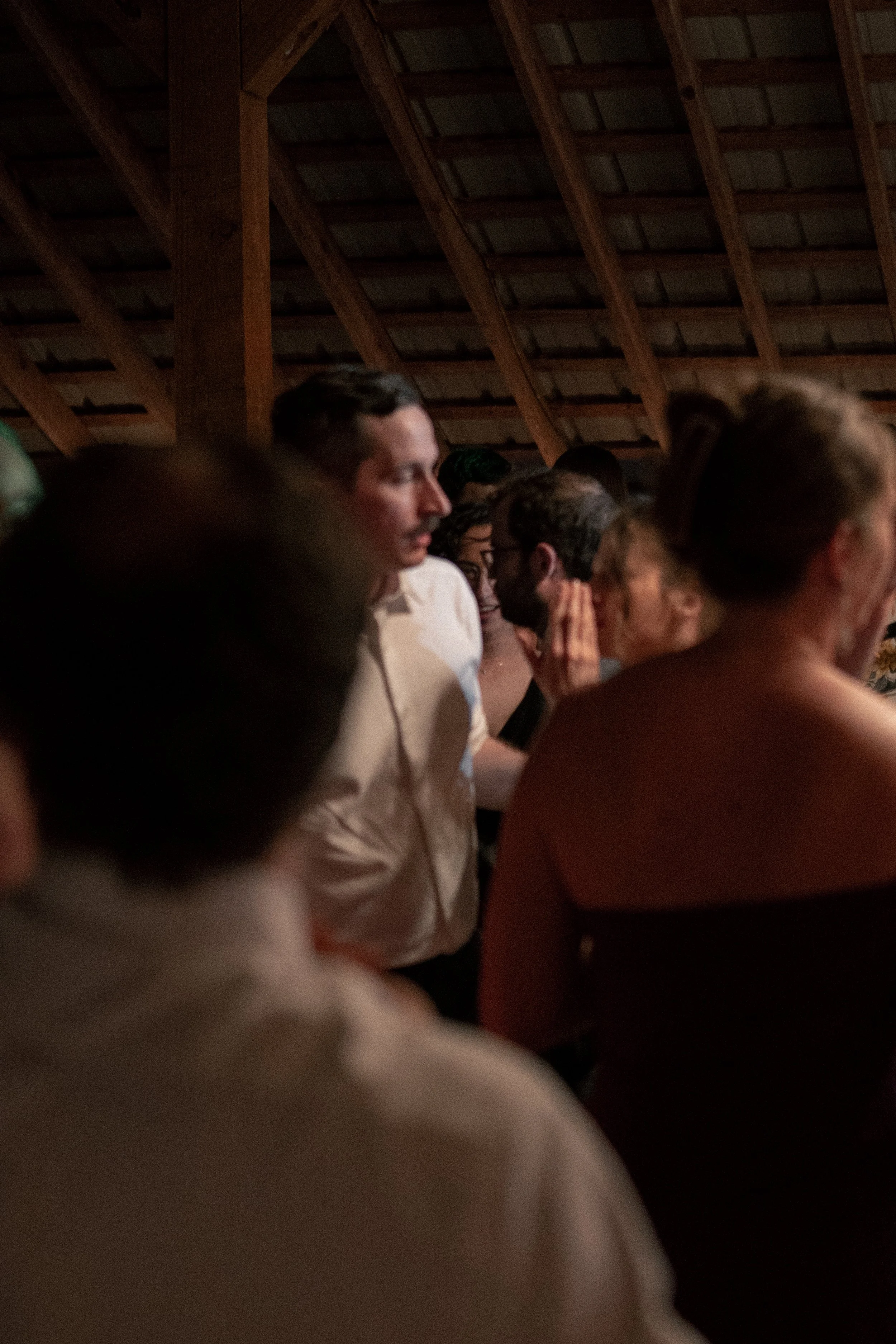 People gathered in a dimly lit indoor space with a high wooden ceiling, appearing to be engaged in a shared activity or event.