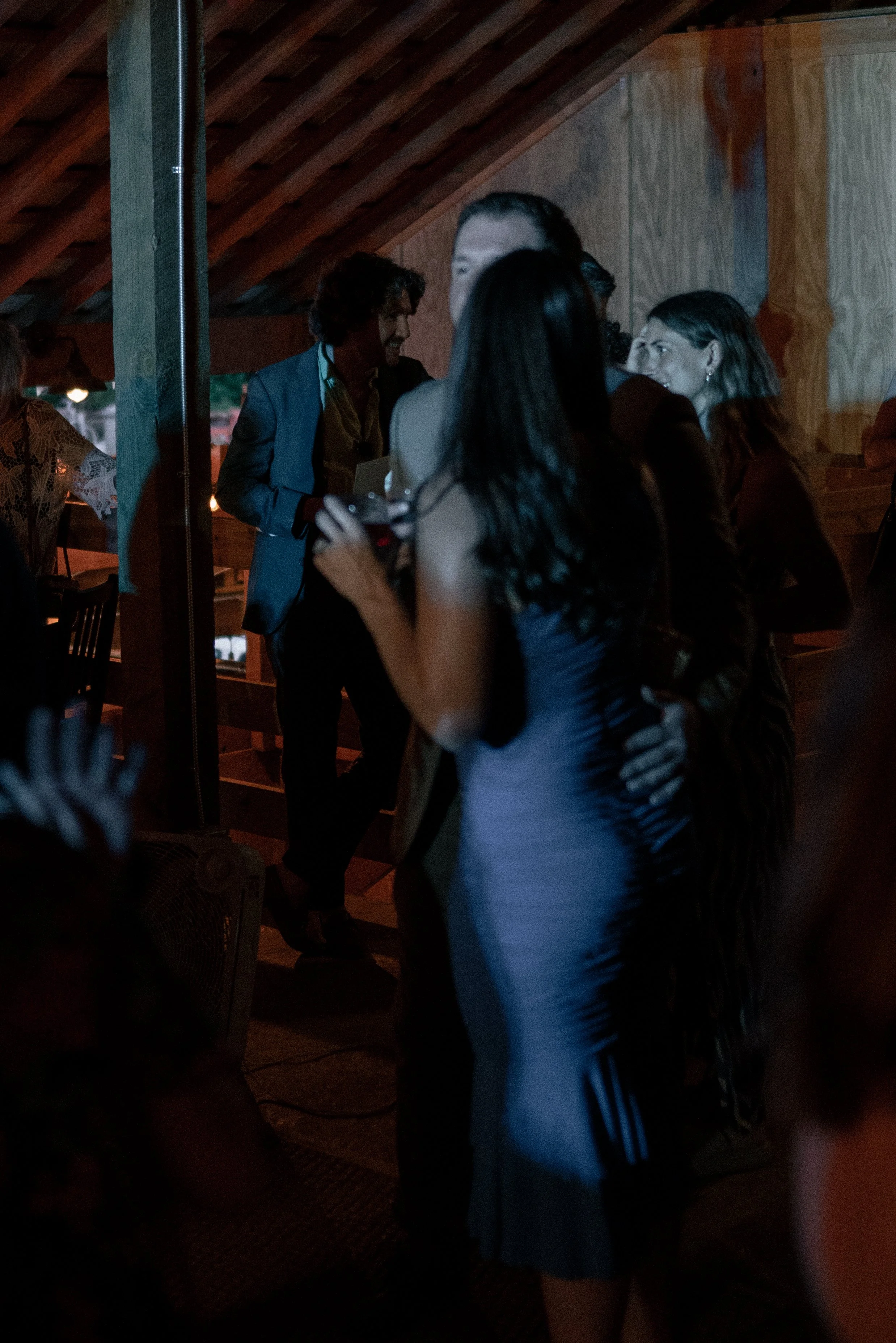 Group of people socializing indoors under a wooden ceiling, some smiling and engaging in conversation.