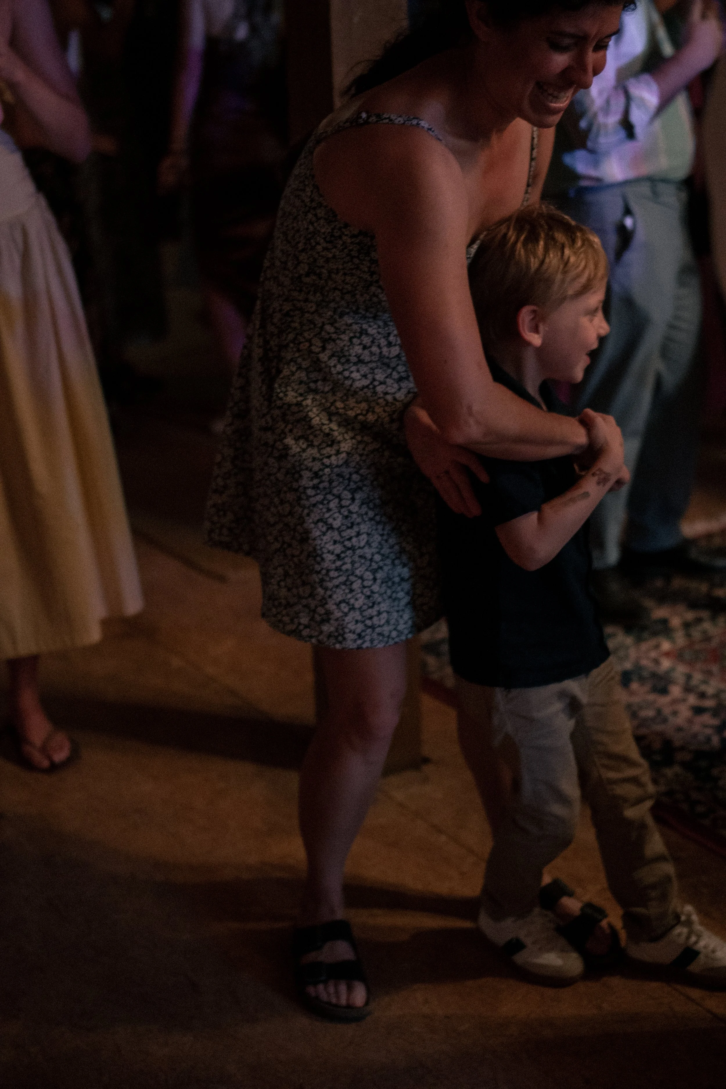 A woman and a young boy dancing closely together indoors surrounded by other people.