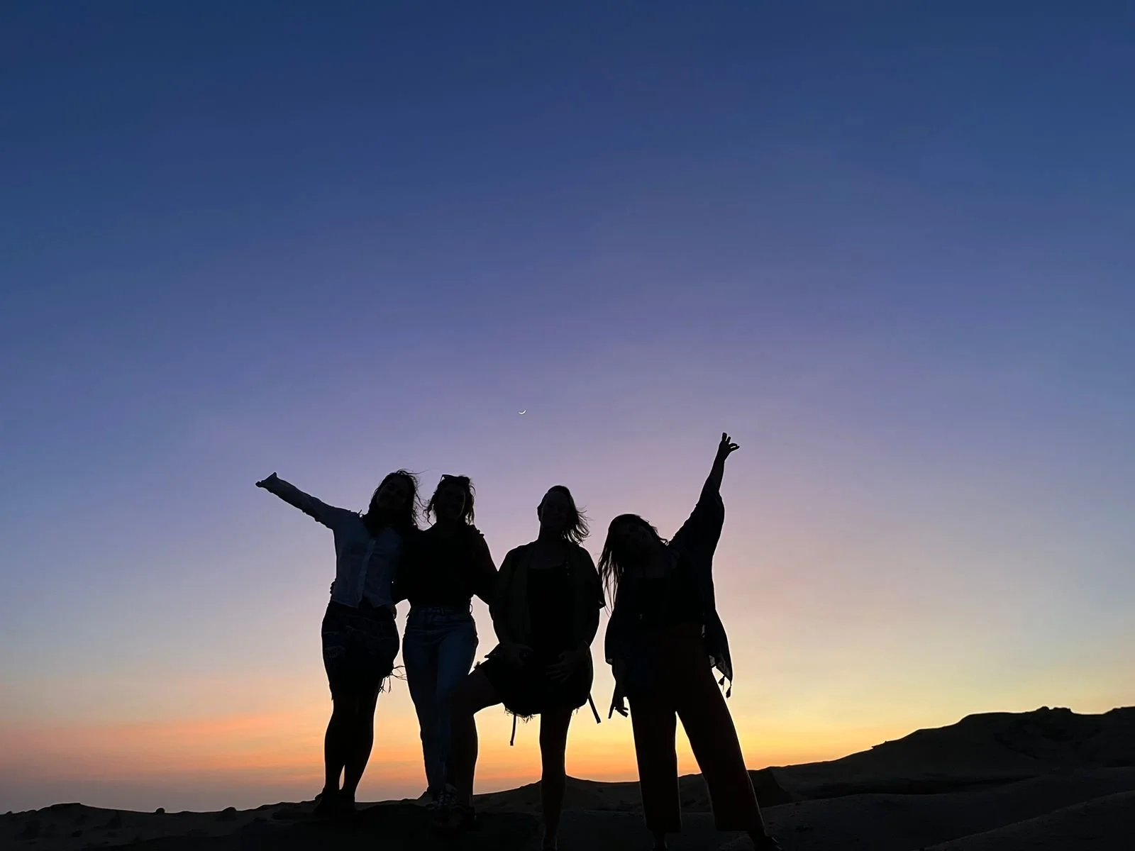 Four silhouettes of adventurous women in front of a sunrise or sunset