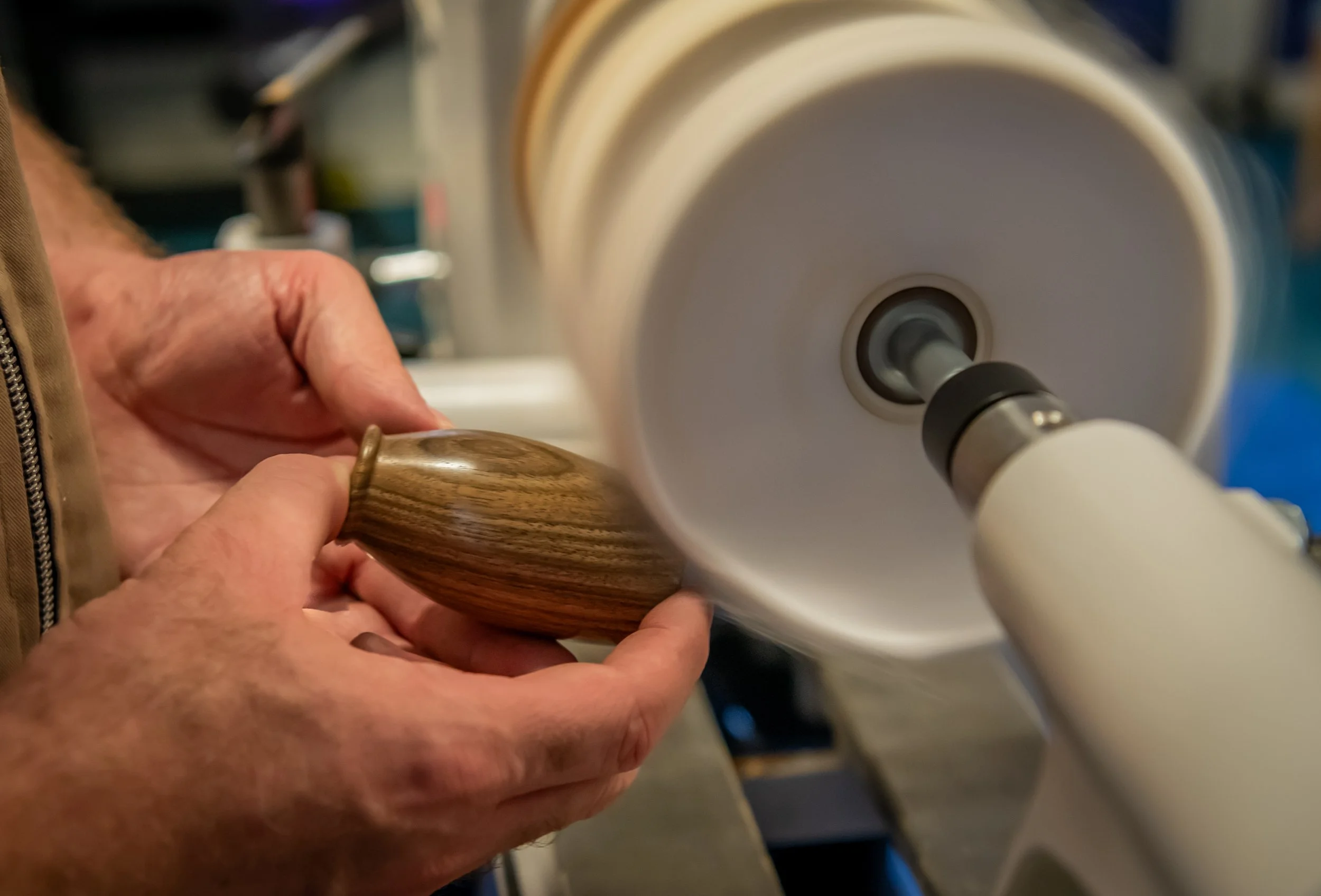 A person shaping wood on a lathe with a focused hand holding the wood while the lathe spins it.