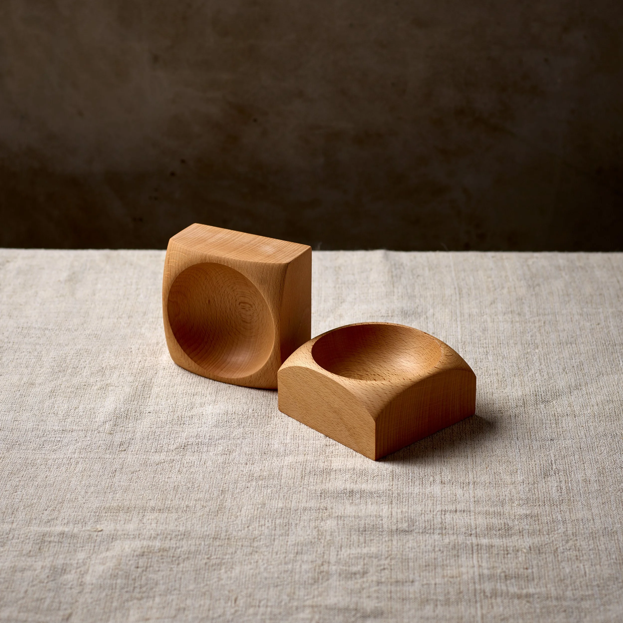 Three wooden bowls of different sizes and shapes on a beige fabric surface, with a dark background.
