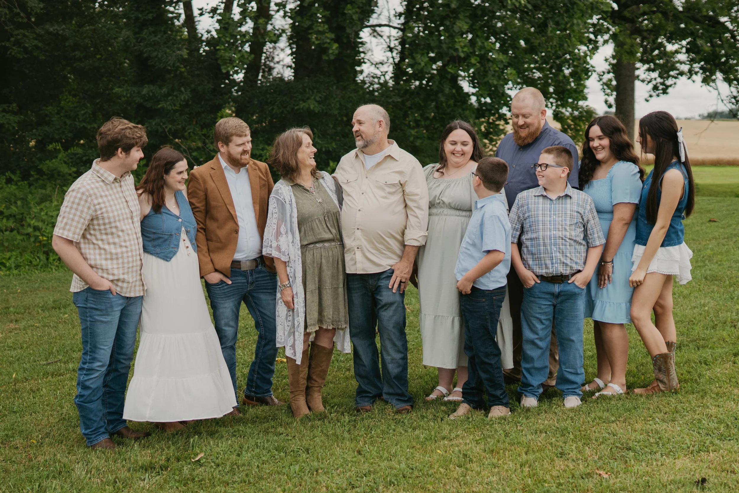 Group of family members smiling and talking outdoors on a grassy field with trees in the background.