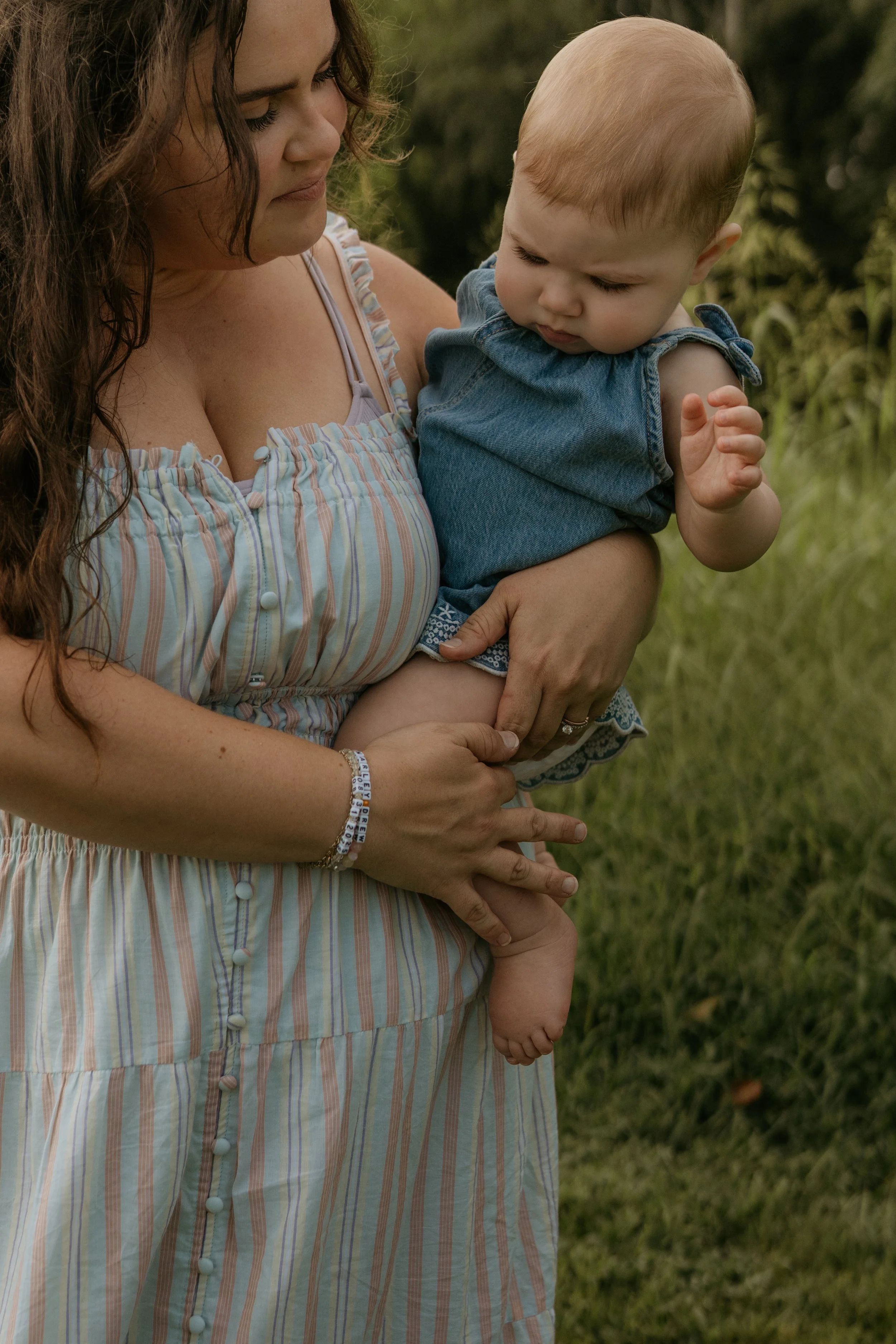 A woman holding a young child in an outdoor setting with green grass and trees.