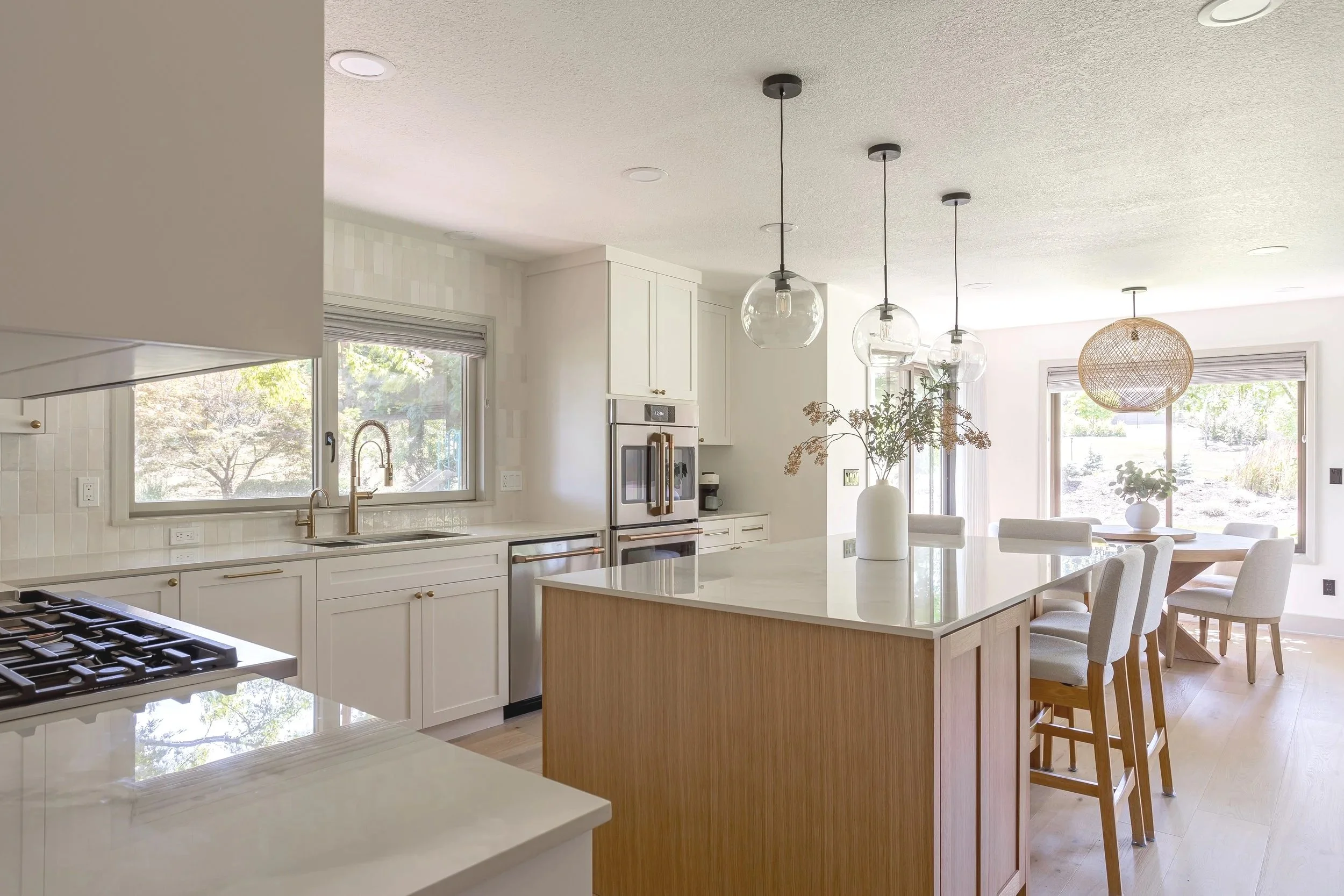 Light-filled kitchen renovation with custom white cabinets, wood island seating, glass pendant lights, and a clean, timeless modern design.