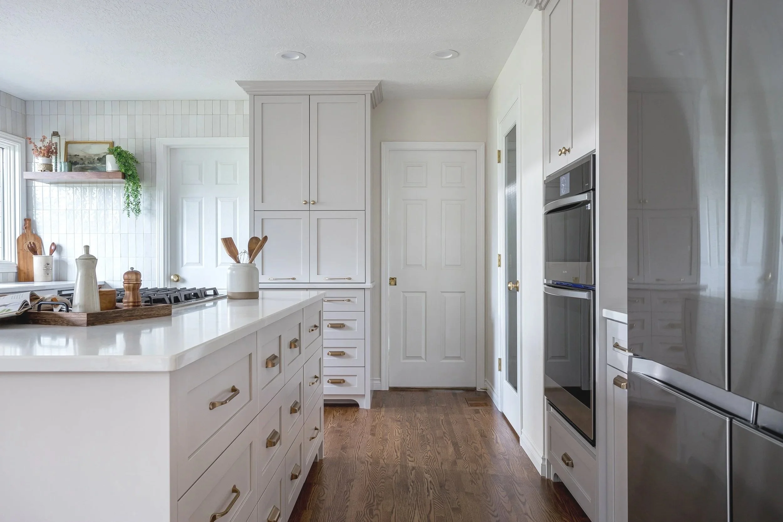 Bright classic white kitchen remodel featuring custom cabinetry with brass hardware, large quartz island, built-in wall ovens, hardwood floors, and a functional layout designed for a modern family home in Portland, Oregon.