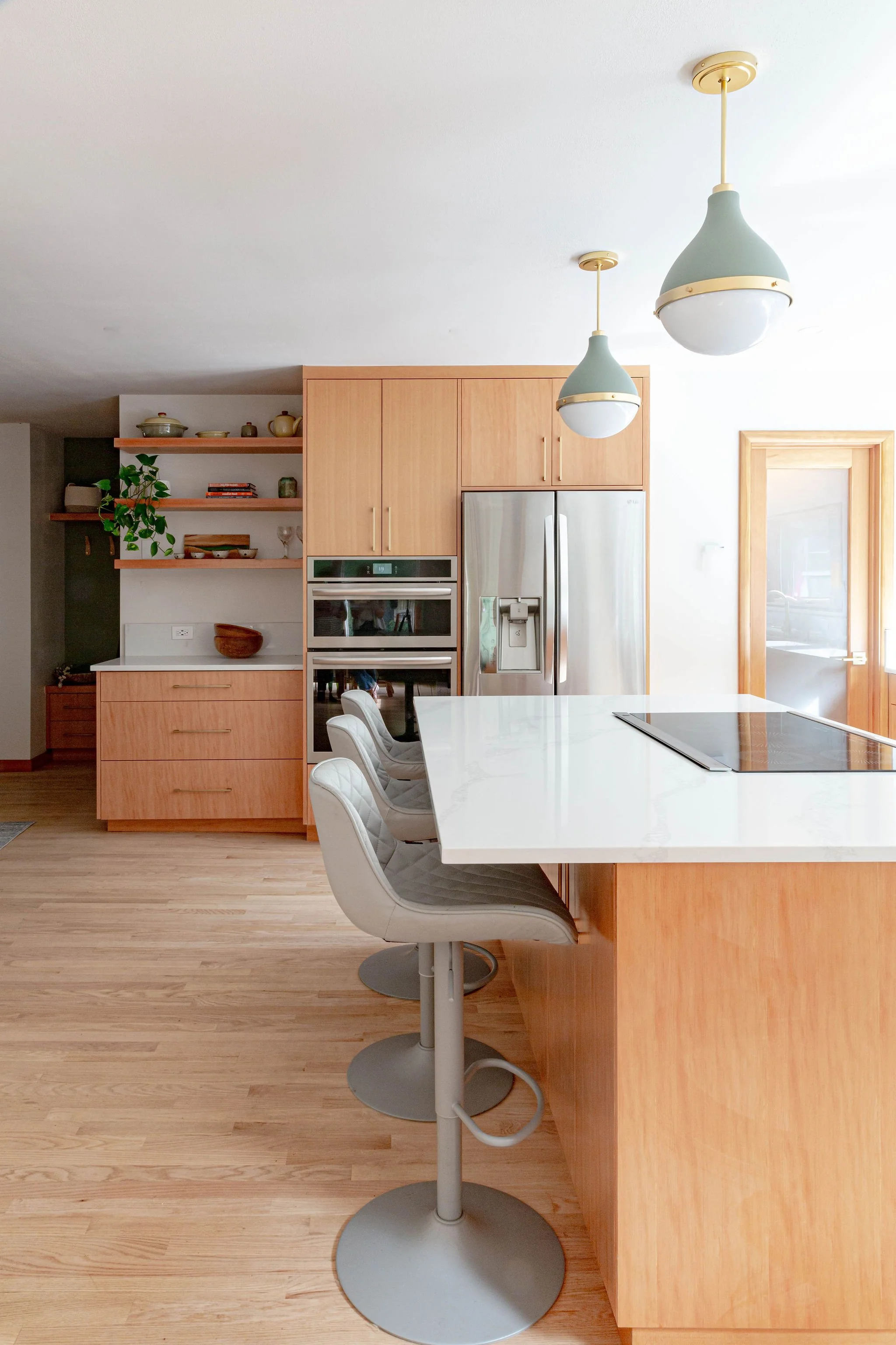 Warm wood kitchen remodel with a central island, modern bar stools, pendant lighting, and natural light from large windows.