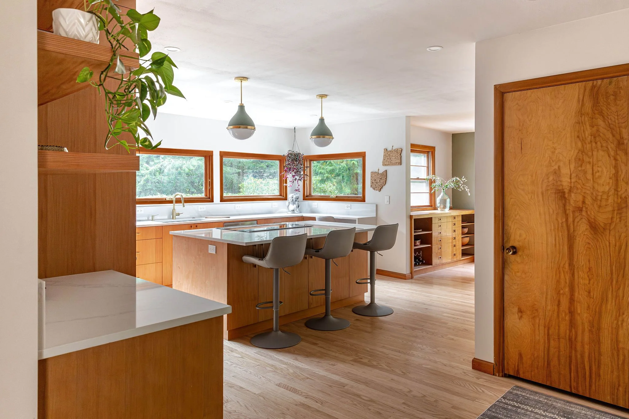 Modern kitchen remodel featuring warm wood cabinetry, a large island with bar seating, pendant lighting, and expansive windows bringing in natural light.