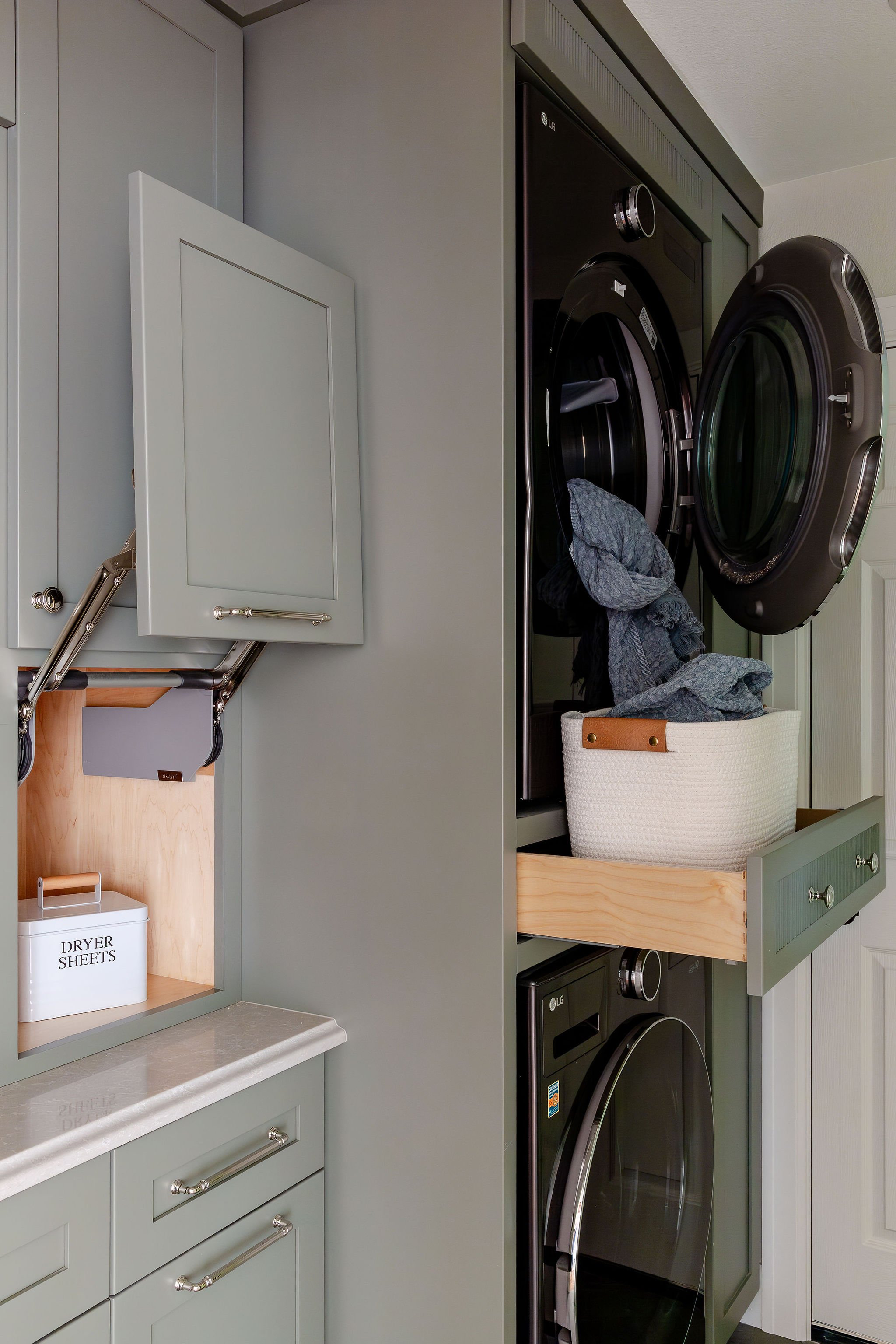 Custom laundry room with sage green cabinetry, built-in washer and dryer, pull-out storage, and smart organization for a modern remodel.