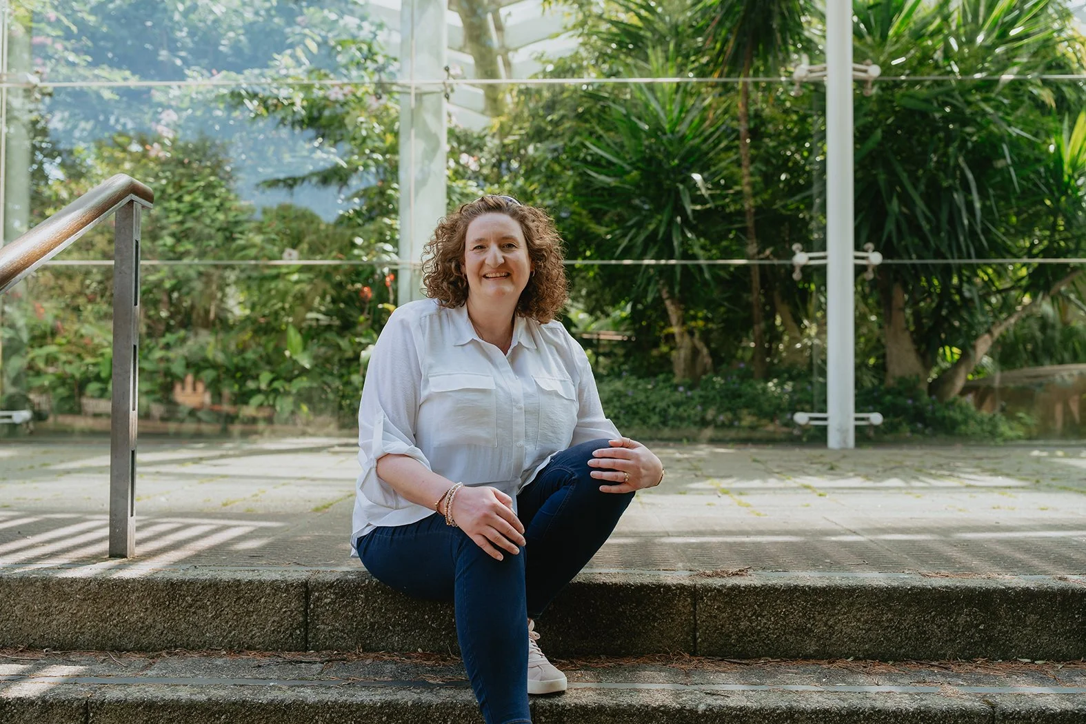 Lucy Kirkman designer sitting on outdoor steps infront of a glass wall and greenery