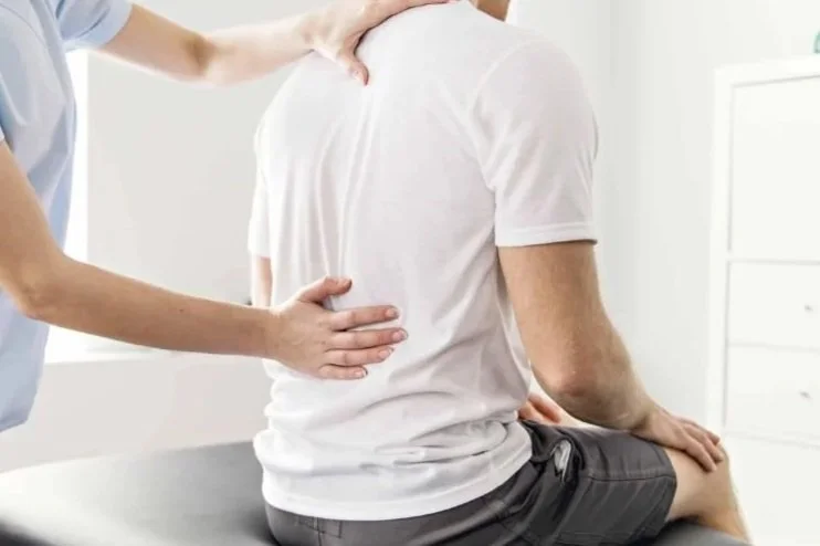 A healthcare professional performing a physical examination on a patient seated on an examination table in a medical office.