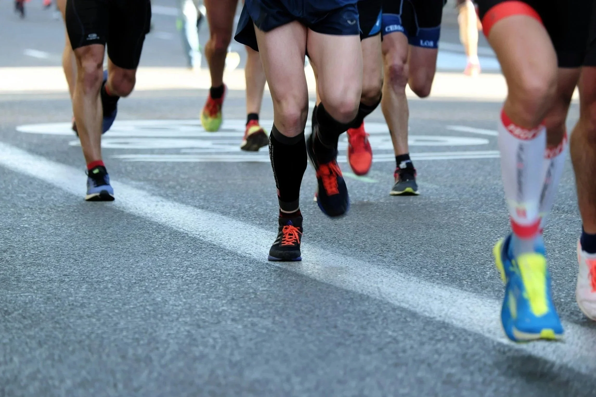 Multiple runners wearing athletic shoes in a race on a city street, viewed from low to the ground.
