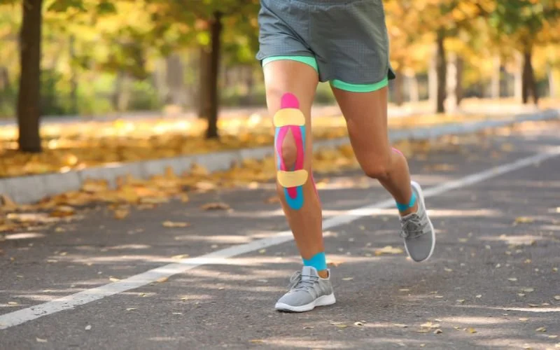 Person wearing athletic shorts running on a park road with colorful adhesive bandages on their leg.