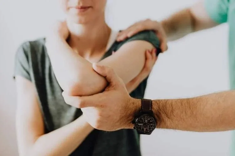 A healthcare professional examines a woman's shoulder, gently holding her arm as part of a medical assessment.