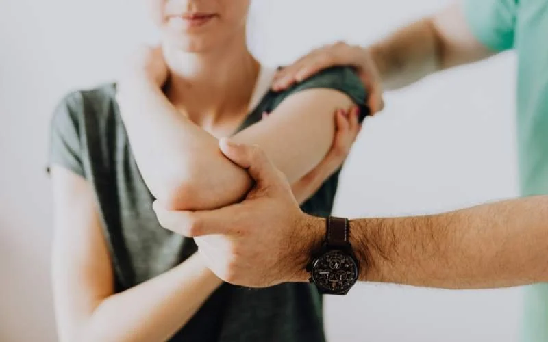 Medical professional examining a woman's shoulder with her arm muscle flexed.