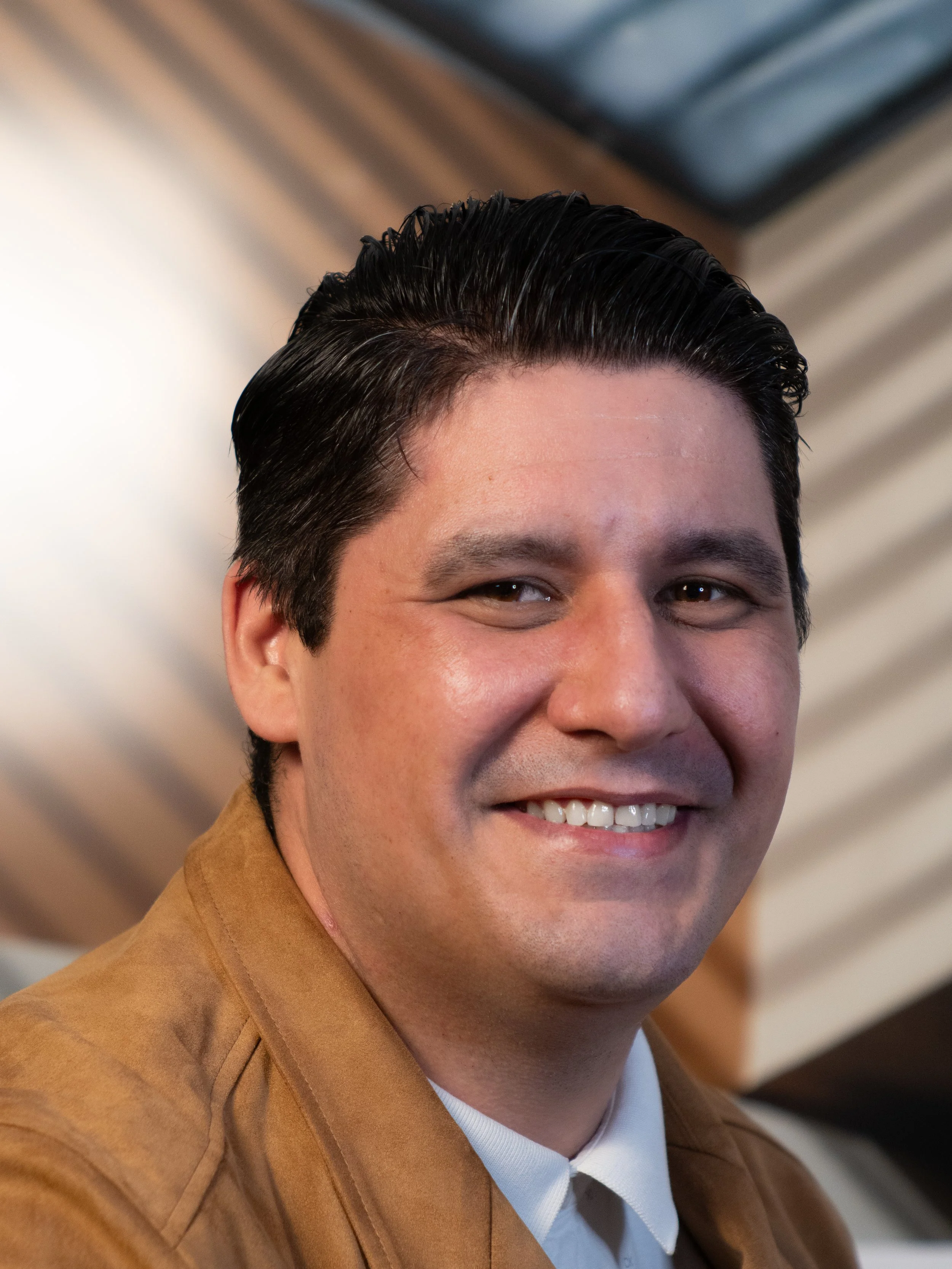 A smiling man in a suit standing in front of a brown and beige background.
