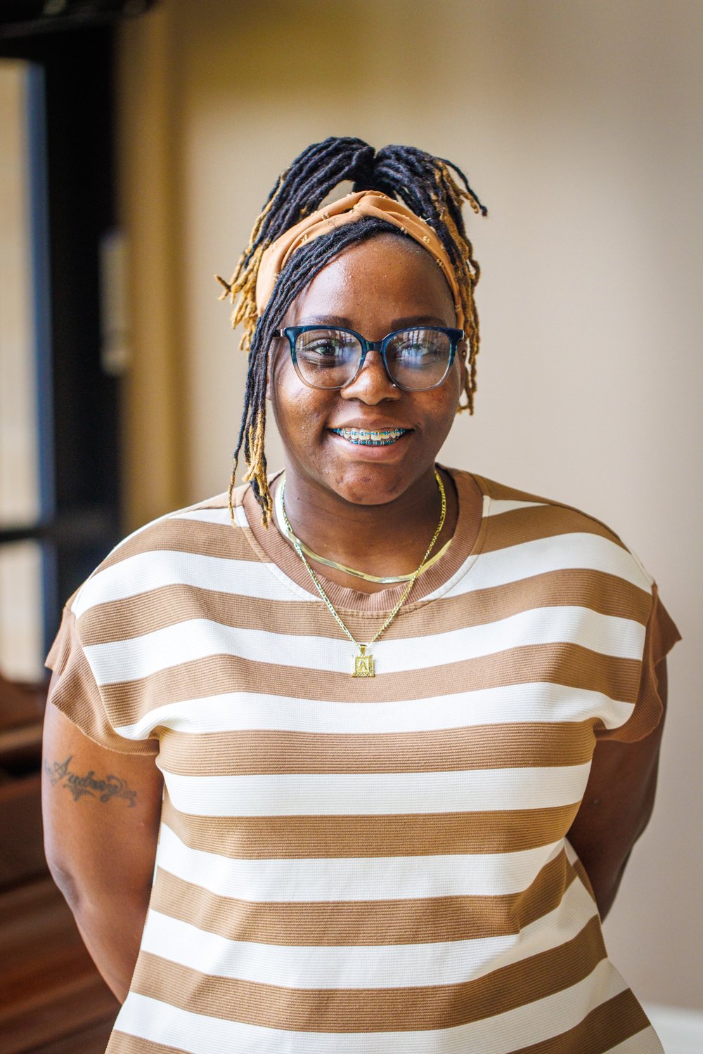 A smiling woman with glasses and dreadlocks, wearing a black blouse with white hearts and a bow tie.