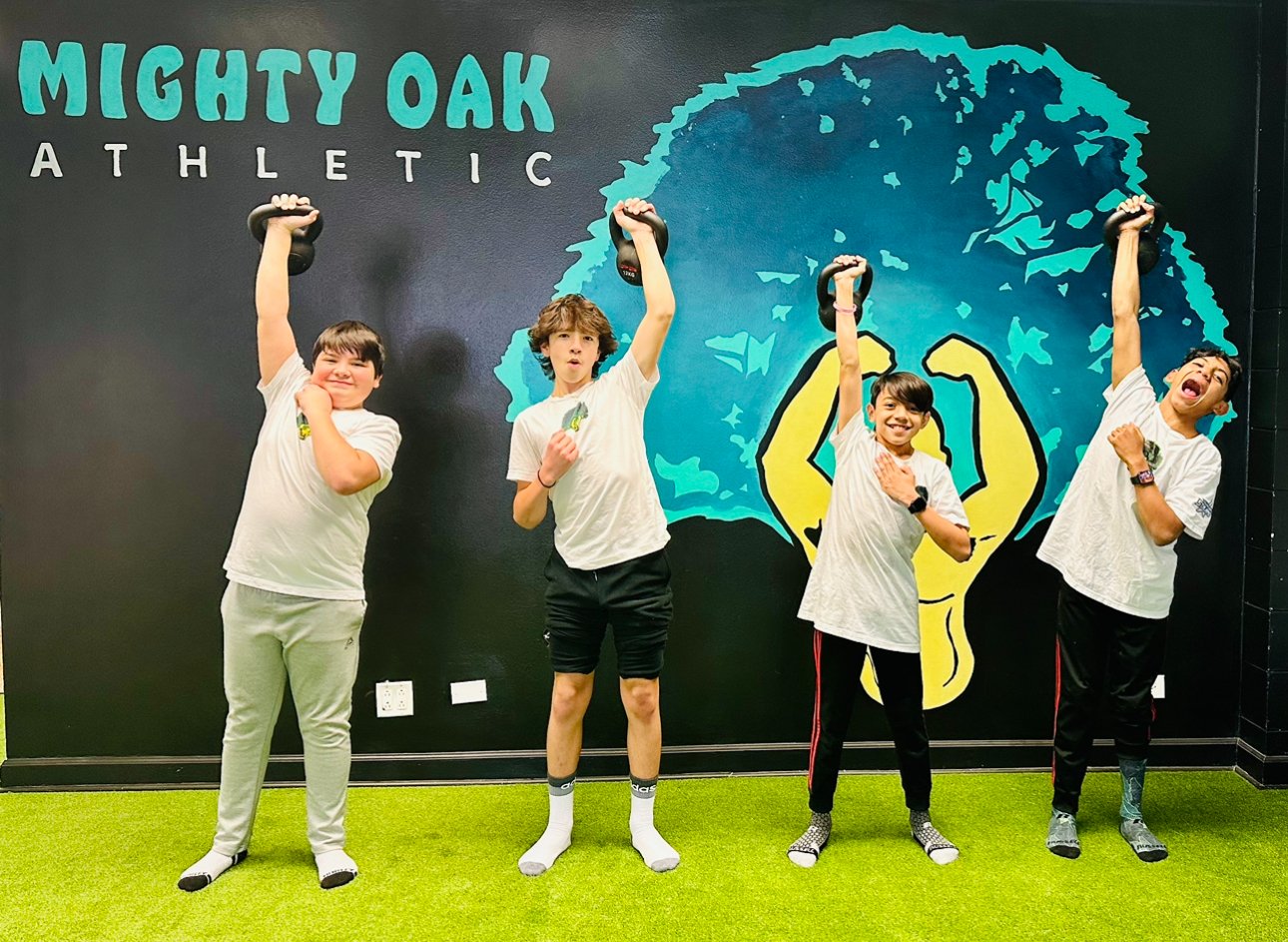Four middle school boys performing a single-kettlebell overhead press at Mighty Oak Athletic — youth strength and agility training in Westmont, IL