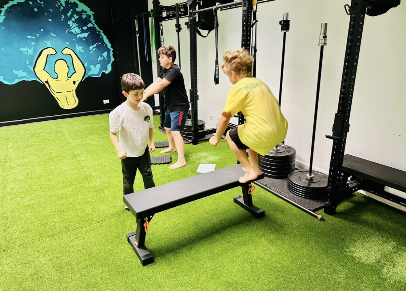Three young athletes training on turf at Mighty Oak Athletic in Westmont, IL, one jumping onto a bench