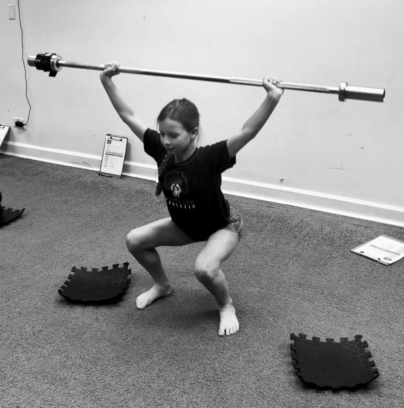 Young girl in a Mighty Oak Athletic shirt performing a barefoot overhead squat with a barbell at the Westmont, IL youth strength gym