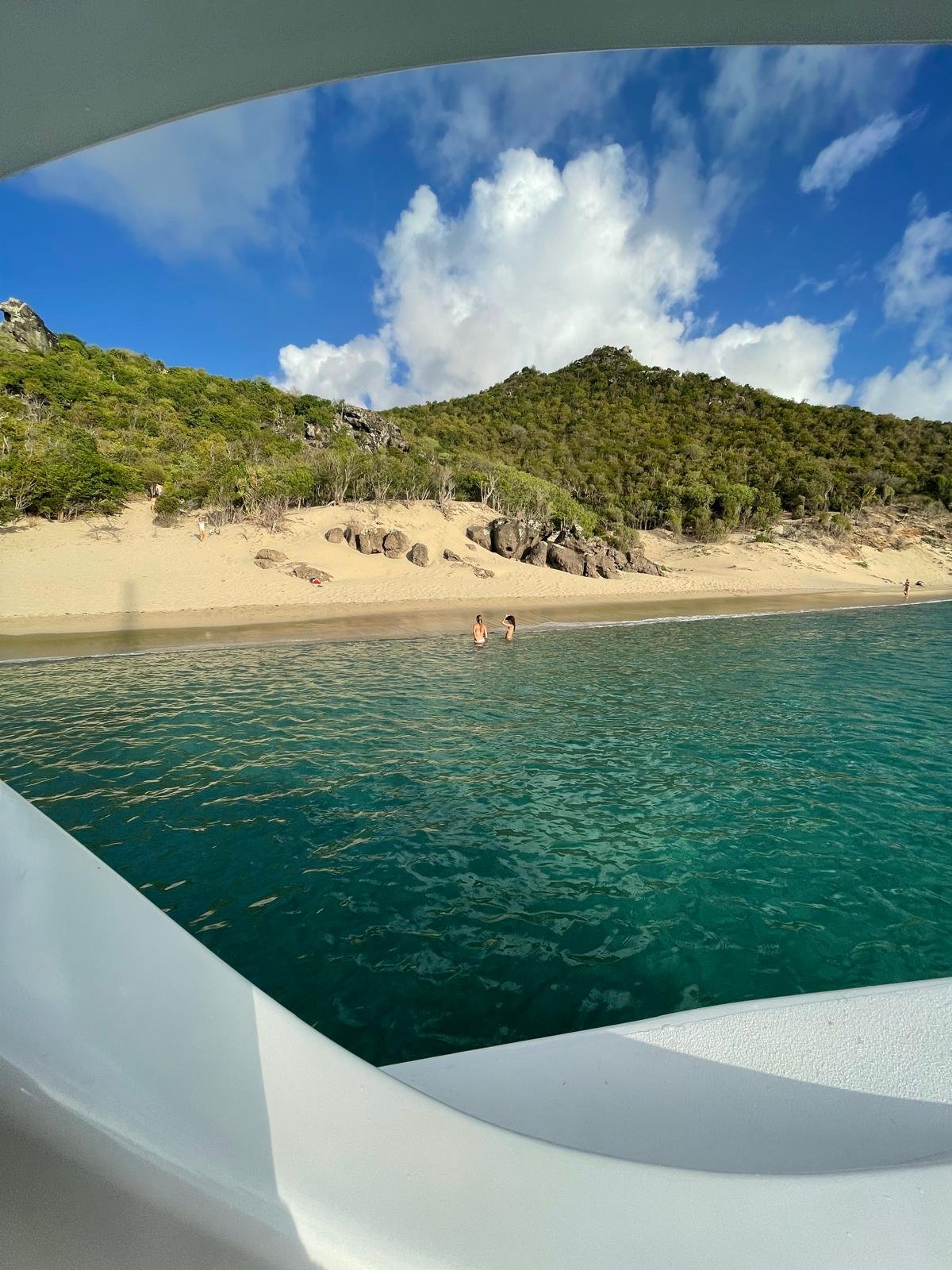 View from the GoodLiving boat of a golden sandy beach and lush green hills in St. Barths during a private Caribbean excursion.