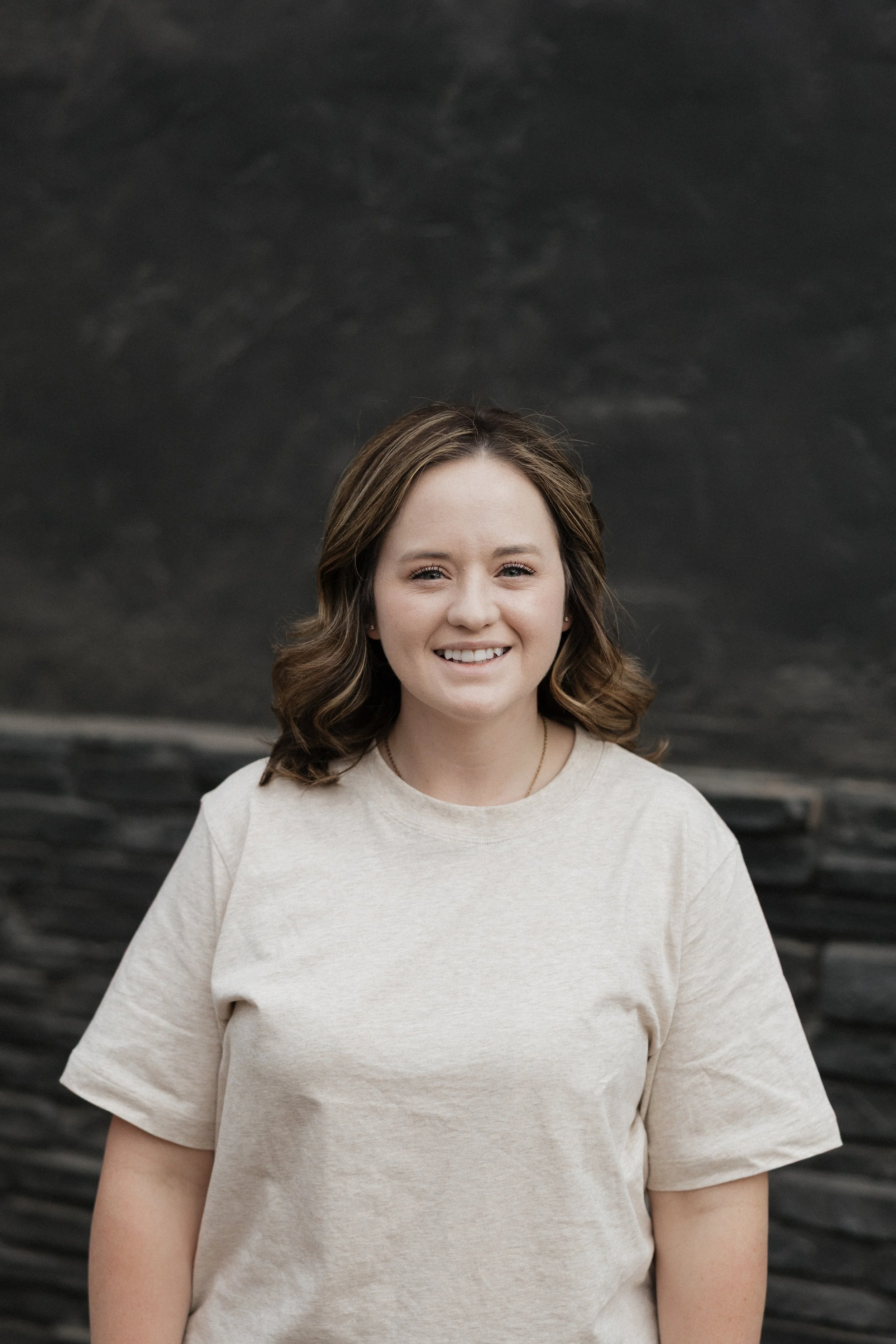 Person smiling in front of a gray brick wall, wearing a maroon top.