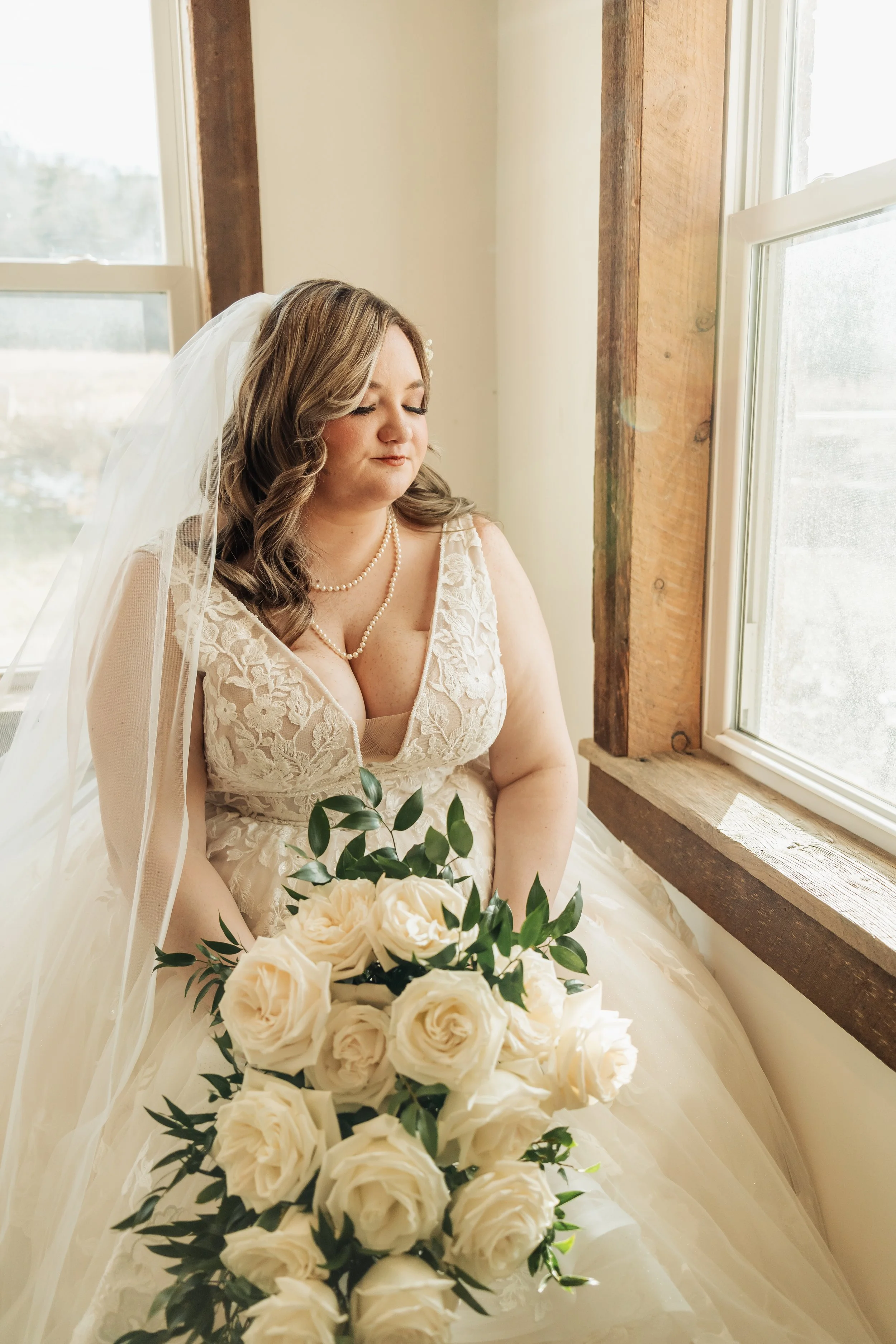 A moody portrait shows a bride posing looking out the window.