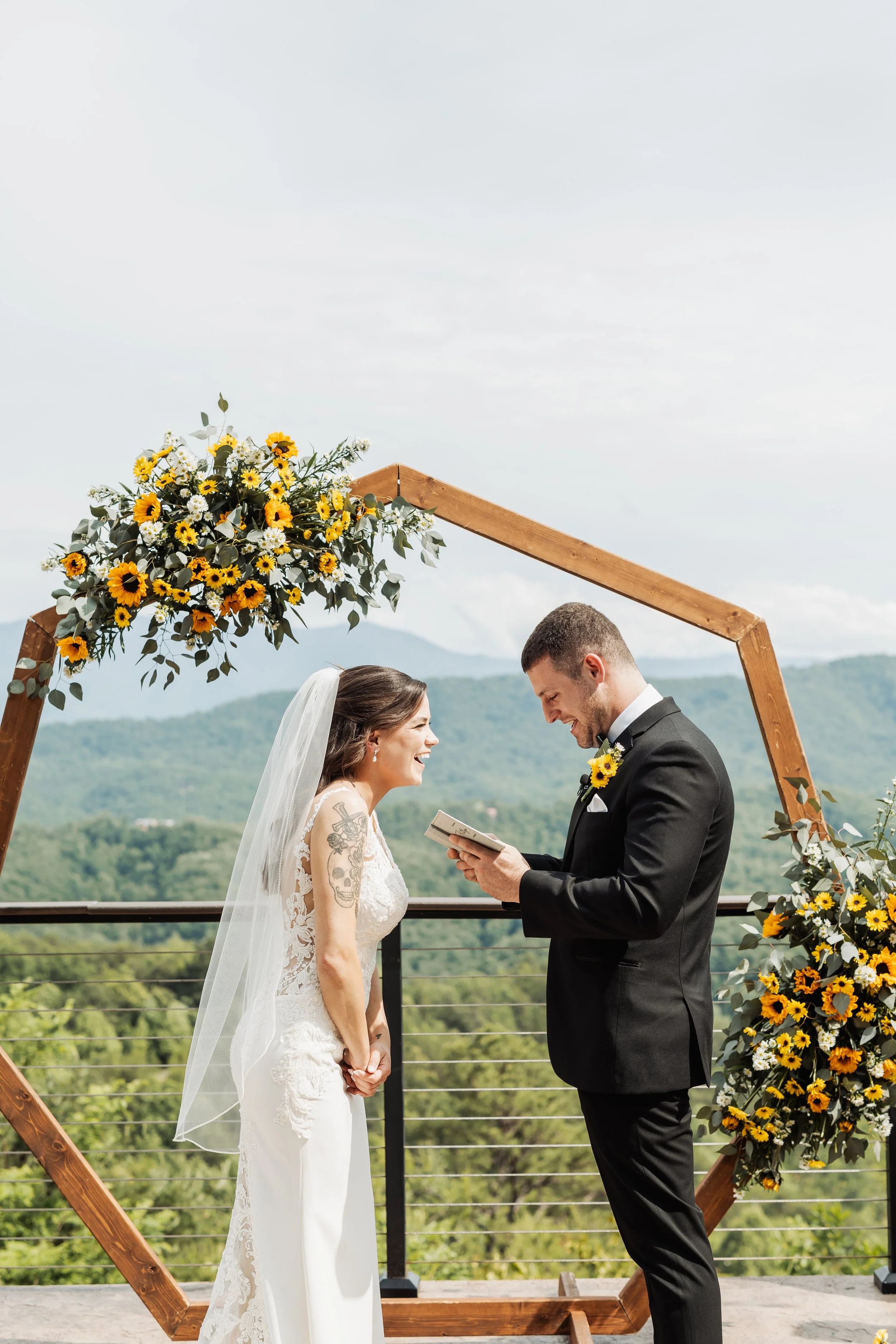 The bride and groom stand in front of their ceremony arch and arch flowers reading vows.