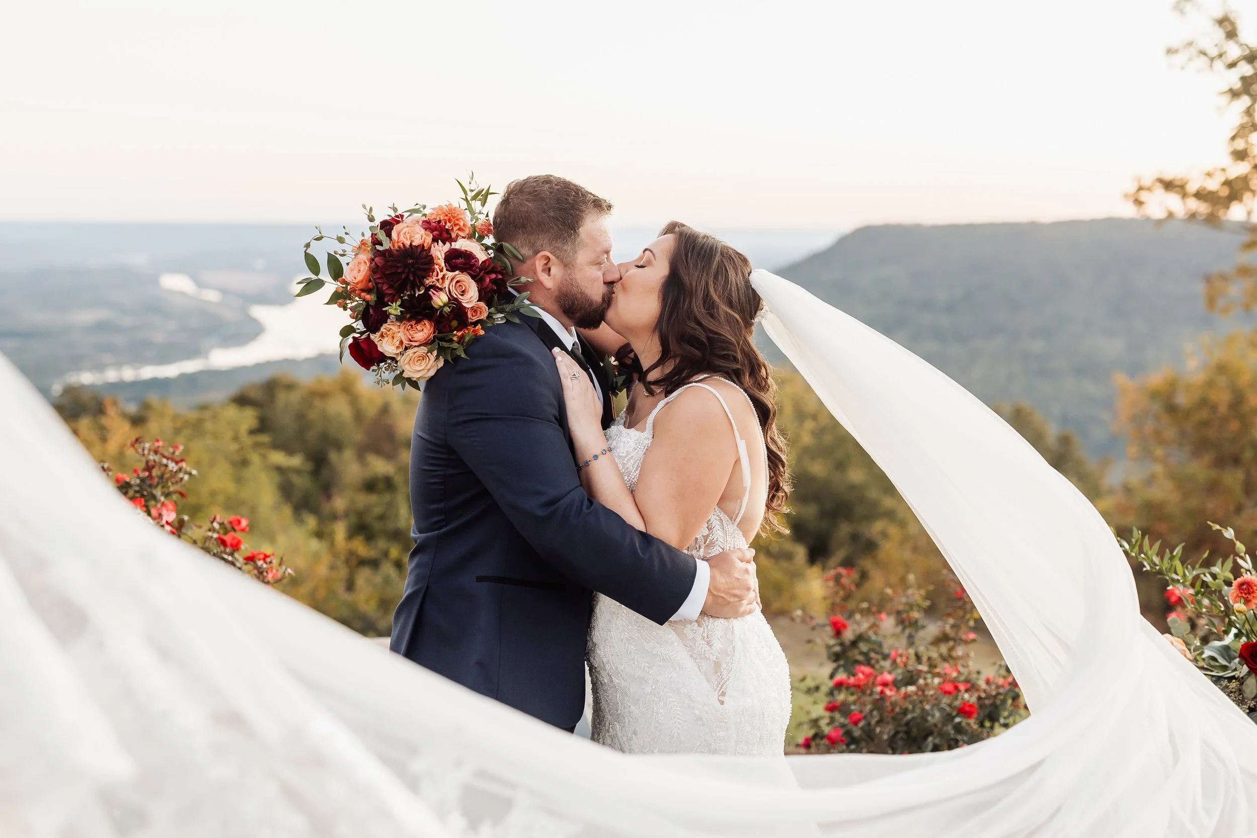 A couple kisses with the veil flying in the wind.