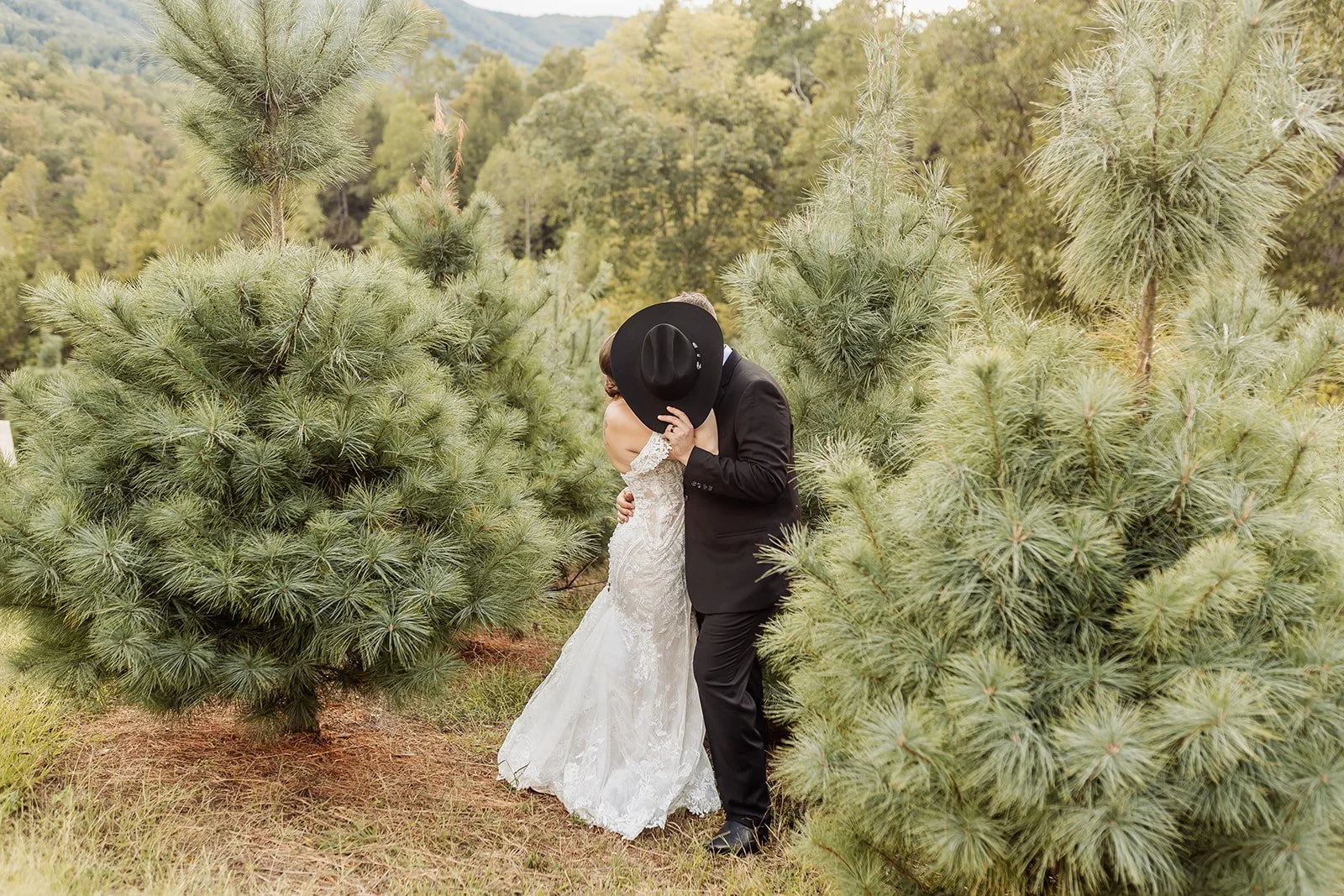The bride and groom hides their face from the camera with a cowboy hat.