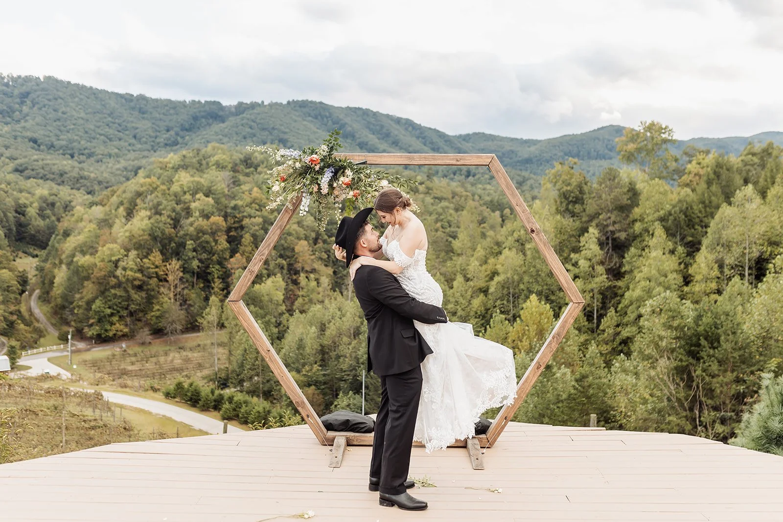 The groom is lifting the bride in front of their ceremony arch, displaying the Smokies in the background.