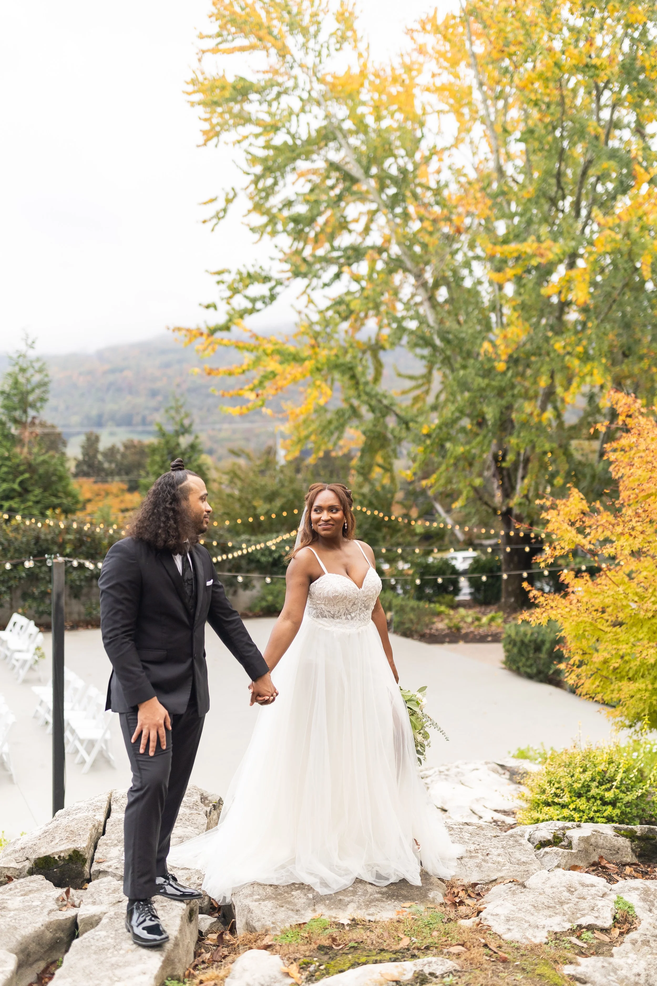 A couple walks across the patio and crosses the string lights.