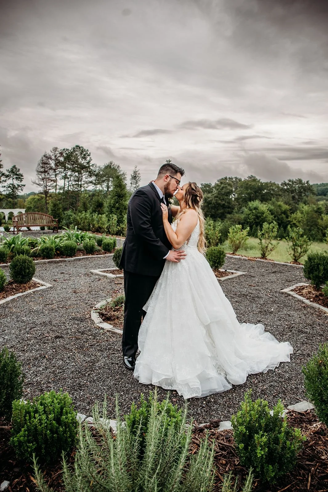 A couple poses in the Woodlands Garden with a dark stormy sky.