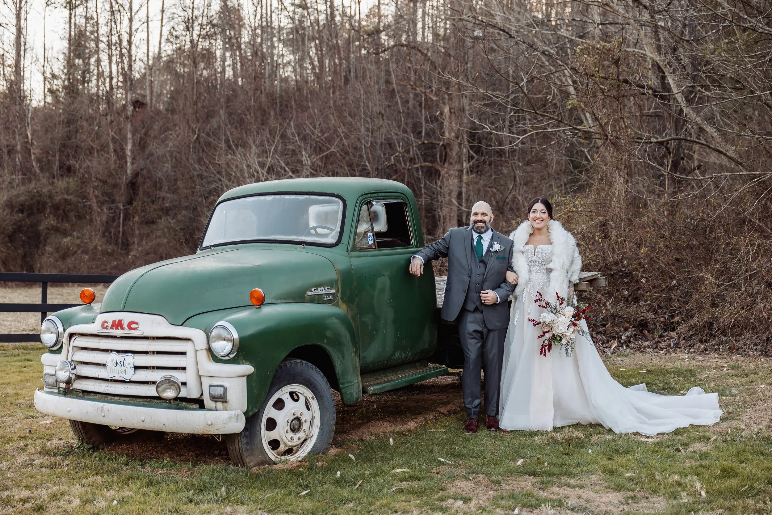 A green truck is to the left of the image with the couple standing to the right leaning on it.