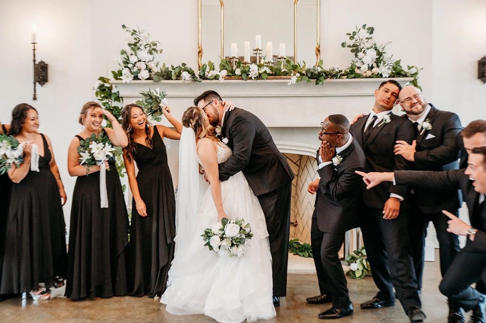 A couple kisses surrounded by their bridal party acting surprised at their ceremony location on-site.