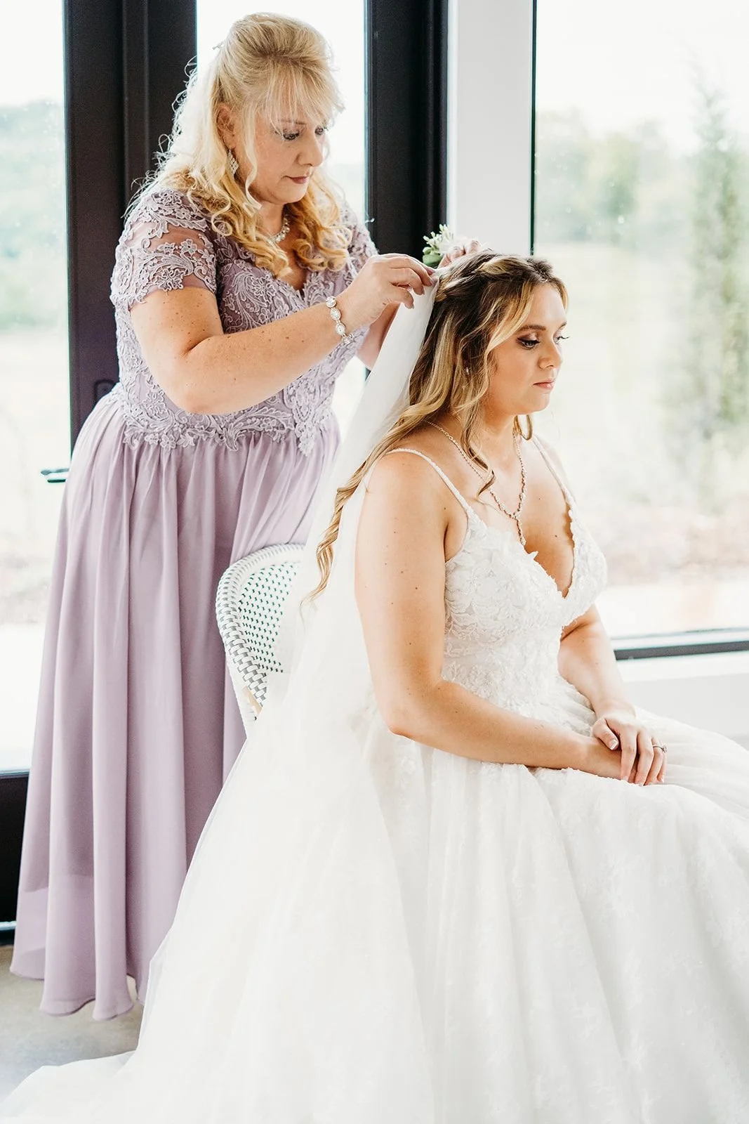 The mom of the bride puts the bride's veil in her hair.