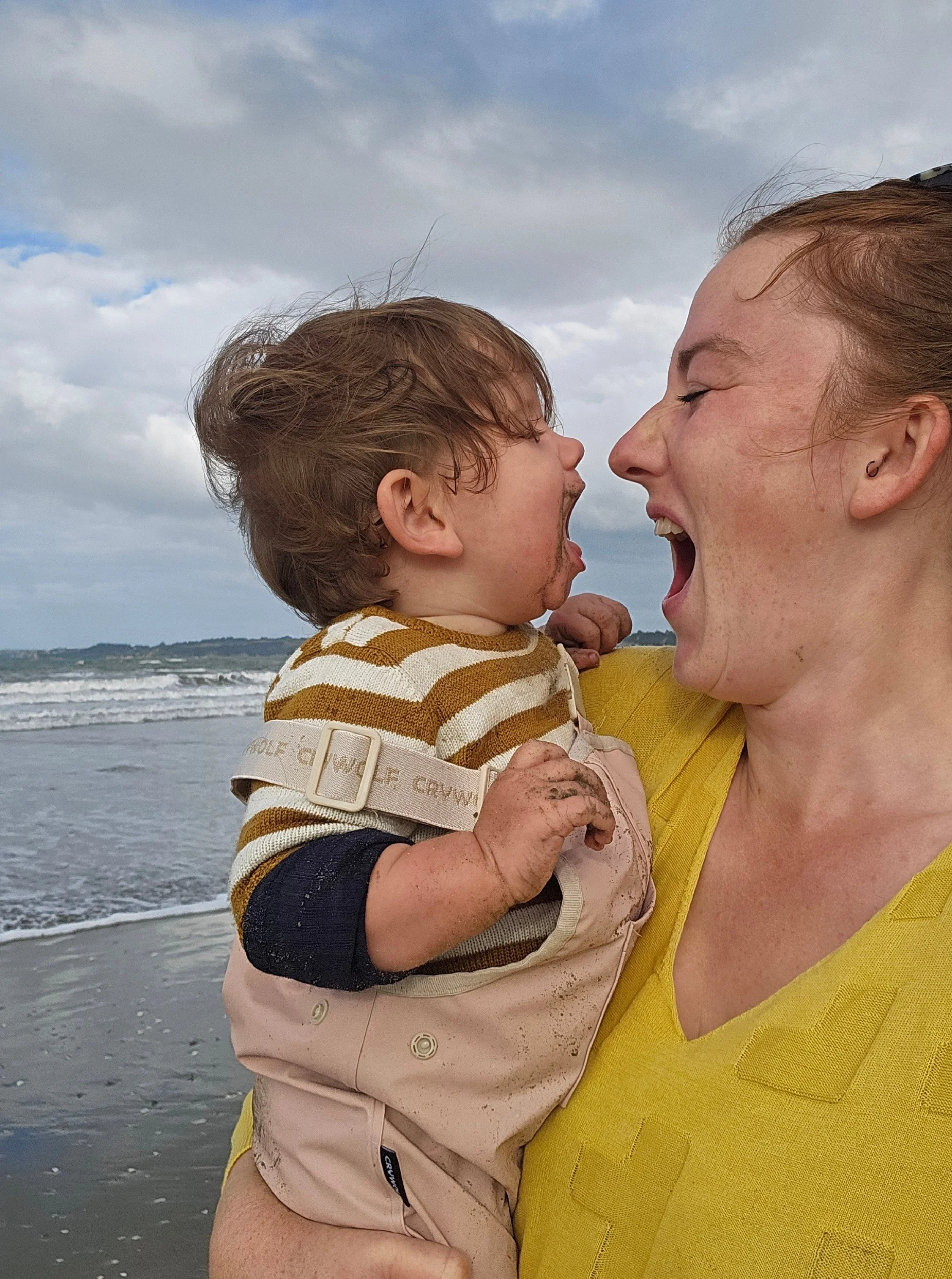 Kate Hall laughing with her daughter Orchard at the beach, capturing the joy, connection and presence that comes from prioritising rest, family and sustainable living.