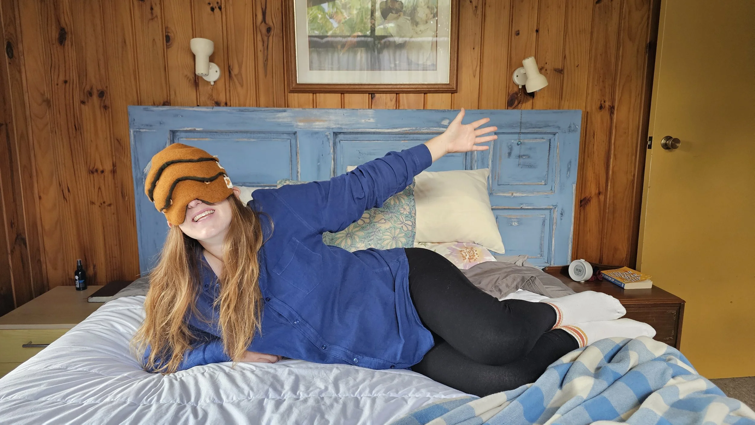 Kate Hall relaxing across a bed while wearing the limited-edition Orchard Orange weighted eye mask from the Ethically Kate × Do Not Disturb collaboration, celebrating the joy of slowing down, resting and protecting your sleep.