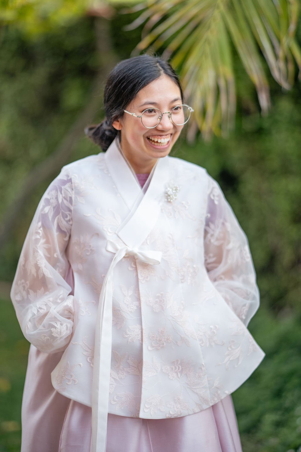 Person wearing traditional Korean hanbok with floral design and glasses, smiling outdoors.