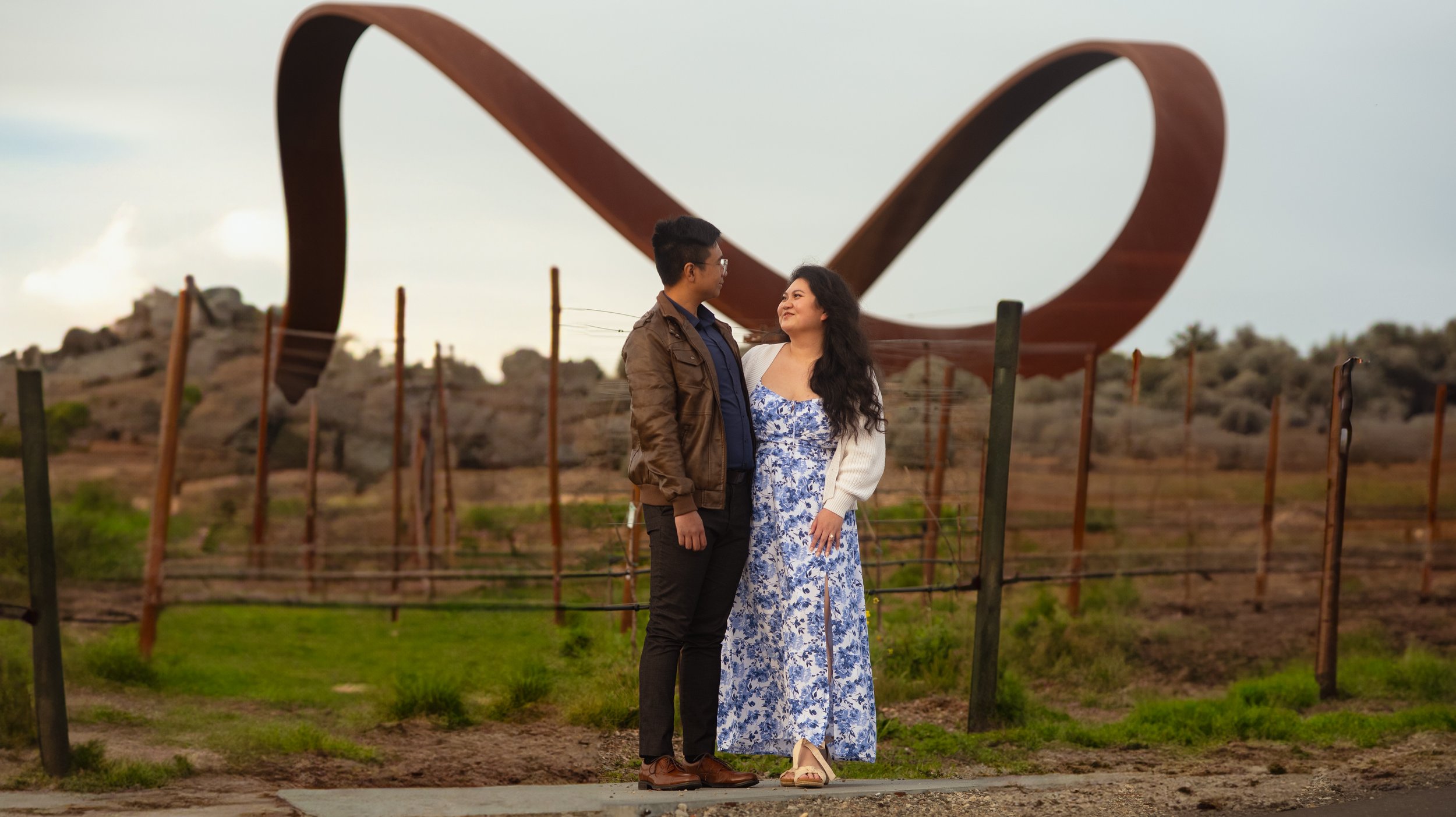 Couple standing in front of large outdoor sculpture in a park