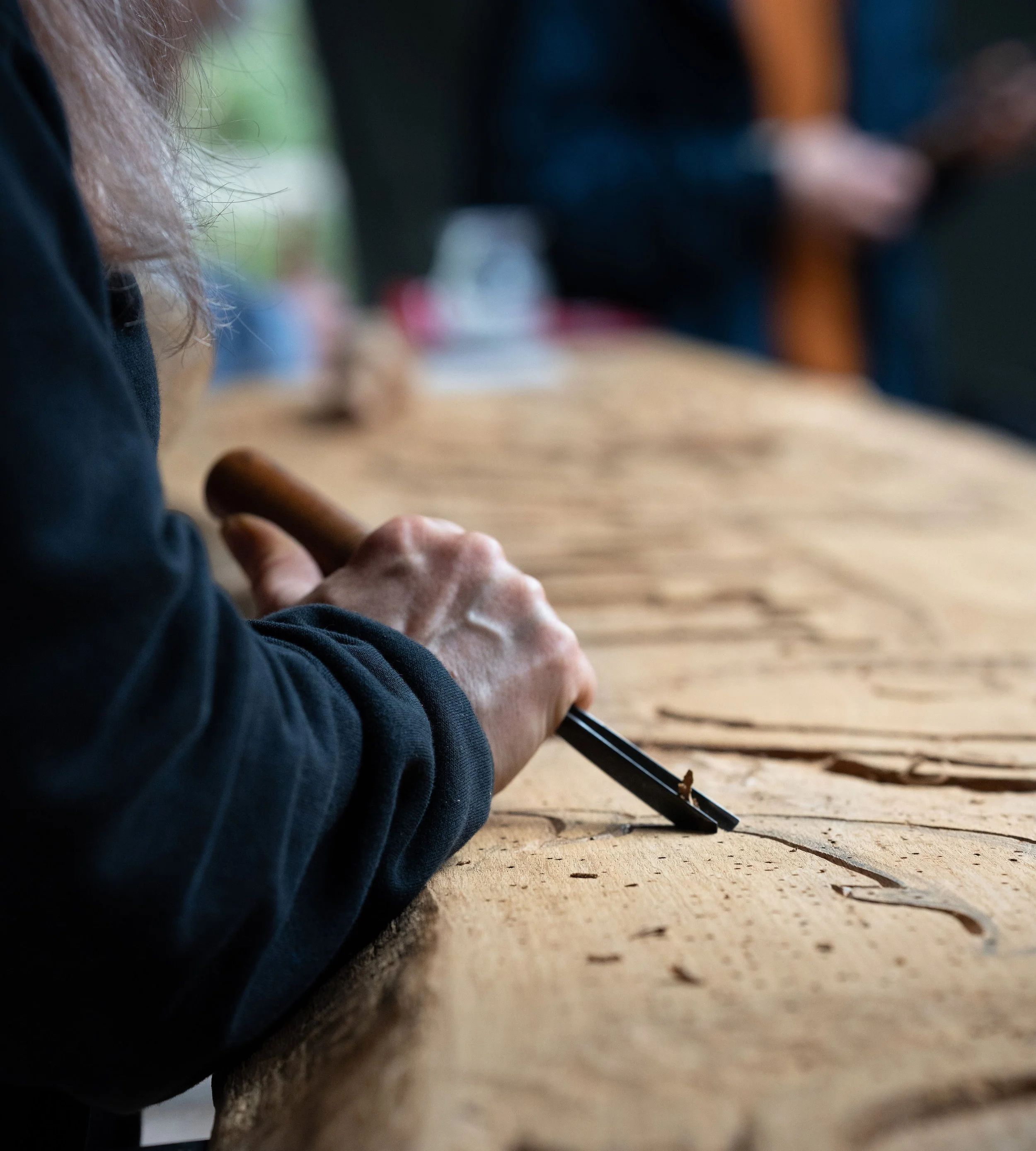 Close-up of a person carving wood with a chisel on a wooden workbench.