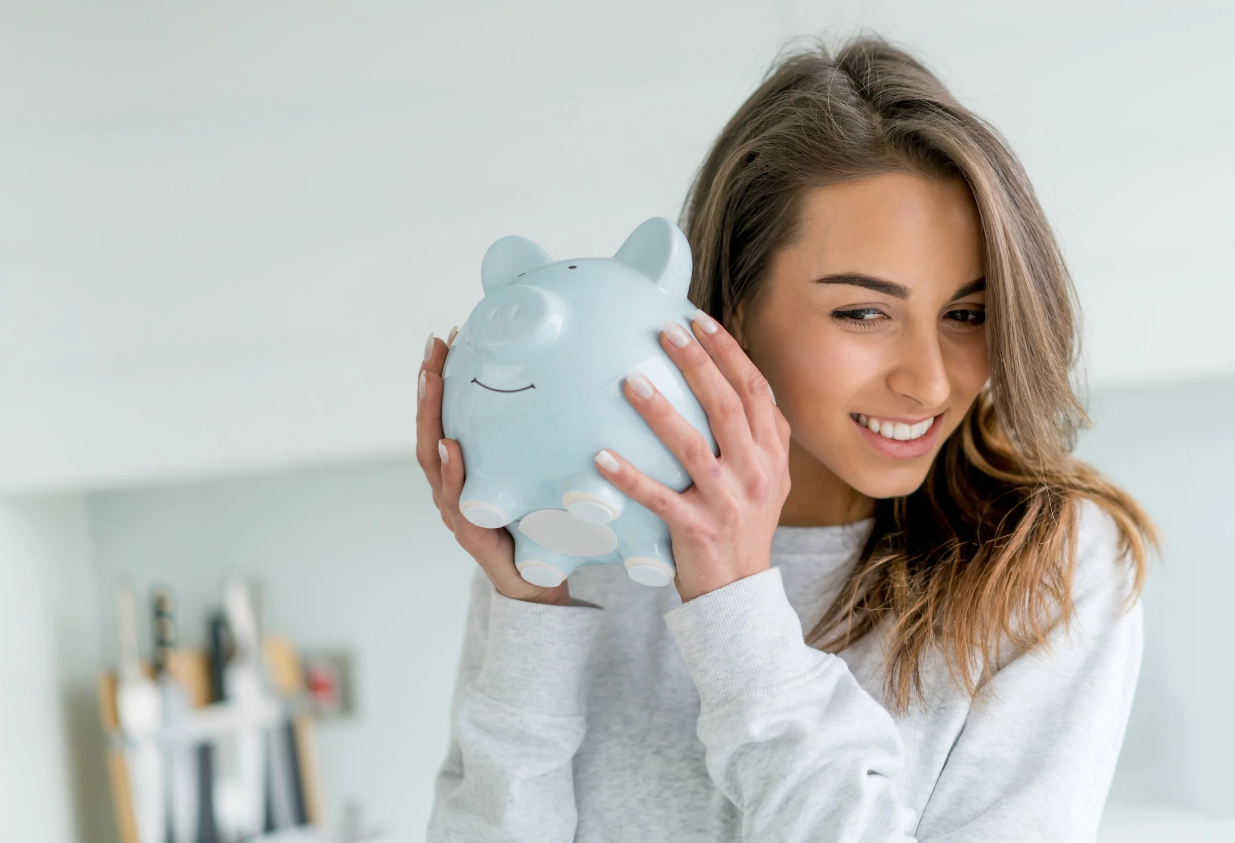 Femme souriante tenant une tirelire en forme de cochon, regardant vers la droite.