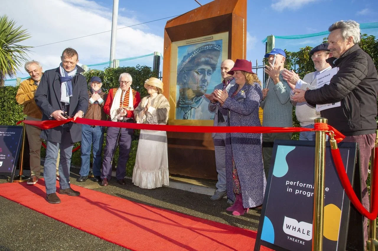 event with local residents and councillors cutting a red ribbon and the launch of corten steel totem on a sunny day