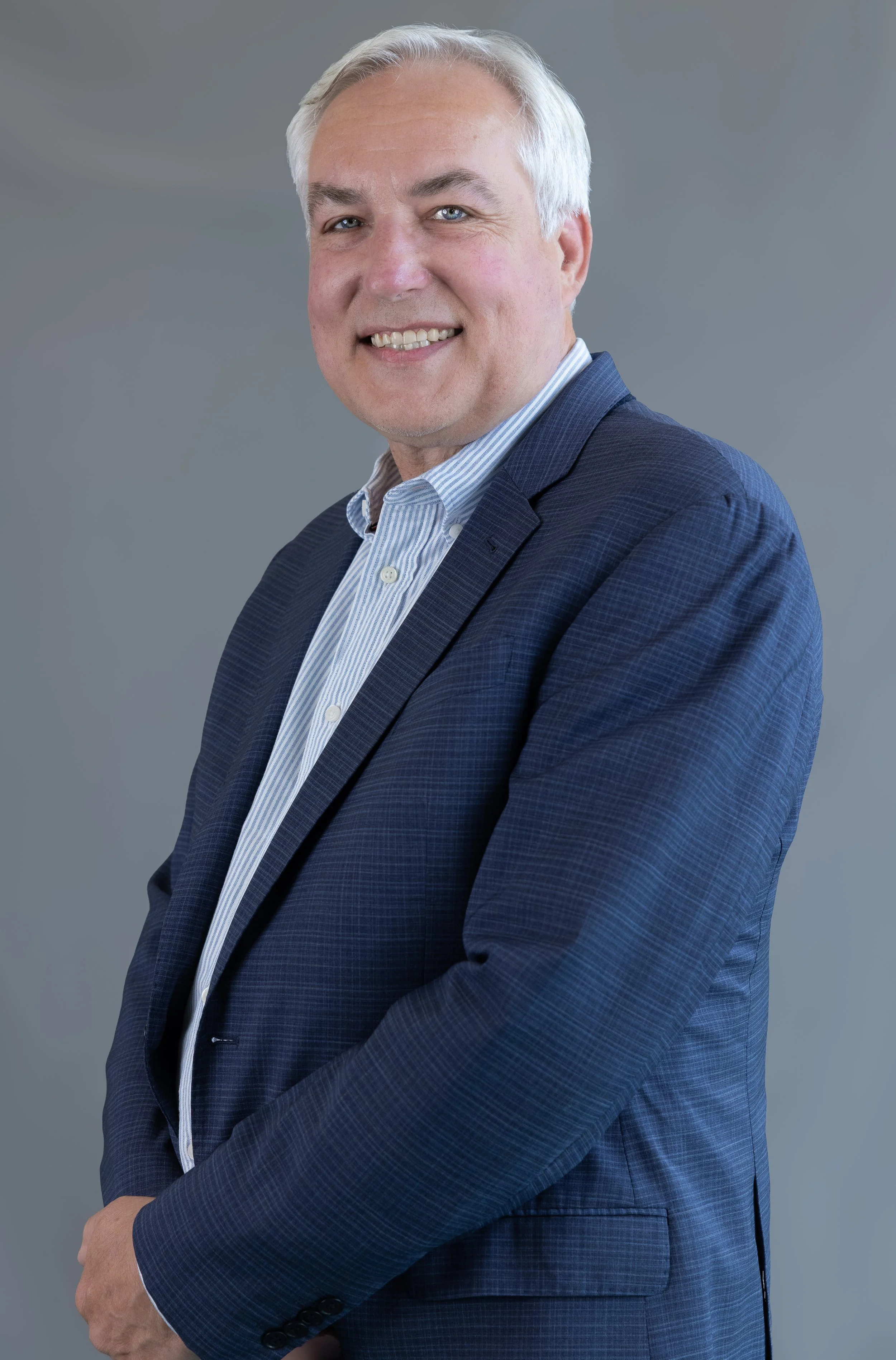 A smiling man with short hair, wearing a collared shirt, in front of window blinds. This is WorldUpstart's mentor, Michael C. Rice.