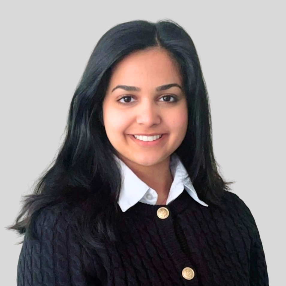 A young woman with shoulder-length black hair, wearing a black textured cardigan with gold buttons over a white collared shirt, smiling in front of a plain light gray background.