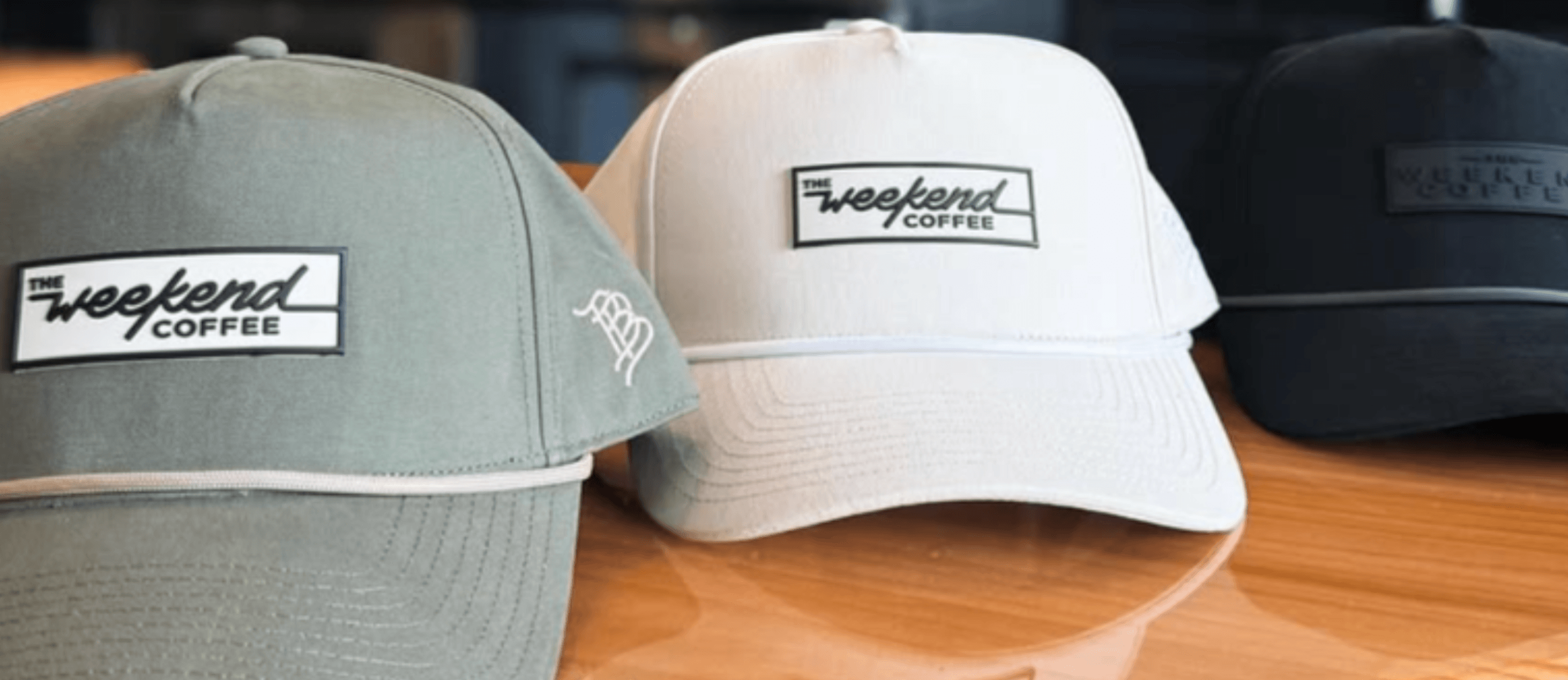 Three baseball caps all with a brand label that reads 'The Weekend Coffee.'
