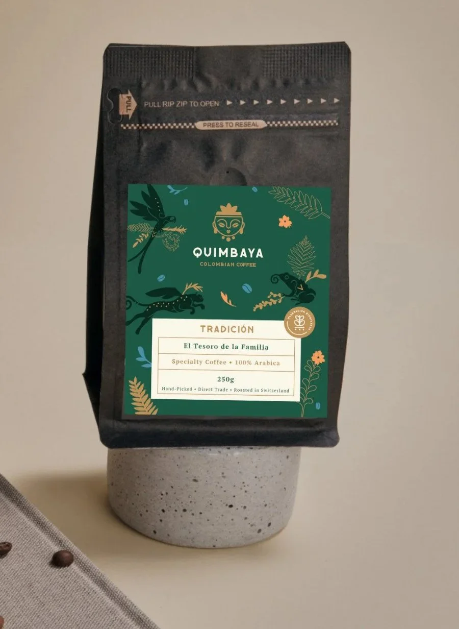 Produktfoto der Quimbaya Tradición Packung von Vicente Espresso mit gruen-goldenem Etikett auf schwarzer Verpackung, stehend auf einem Betonbecher