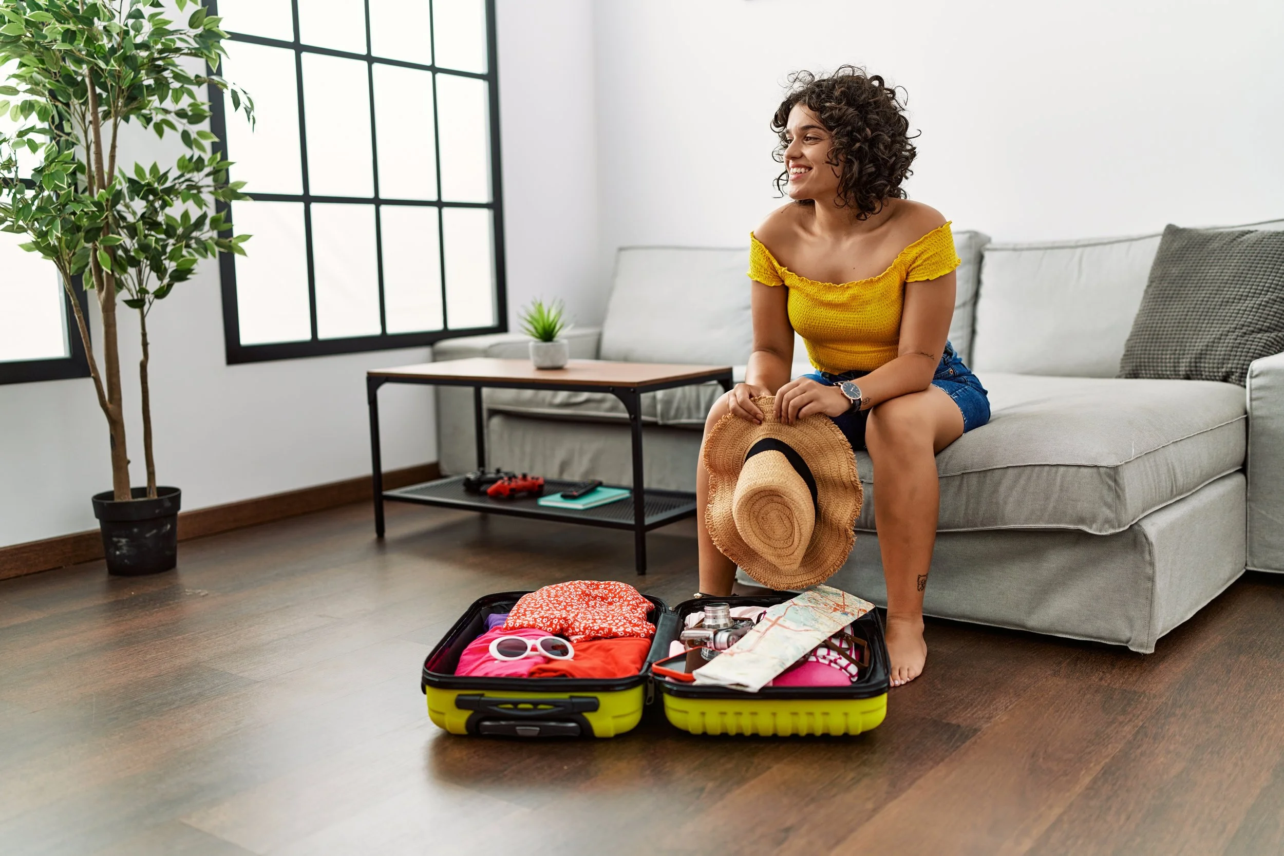 Una mujer dominicana feliz en su sala mientras hace las maletas para viajar a Estados Unidos.