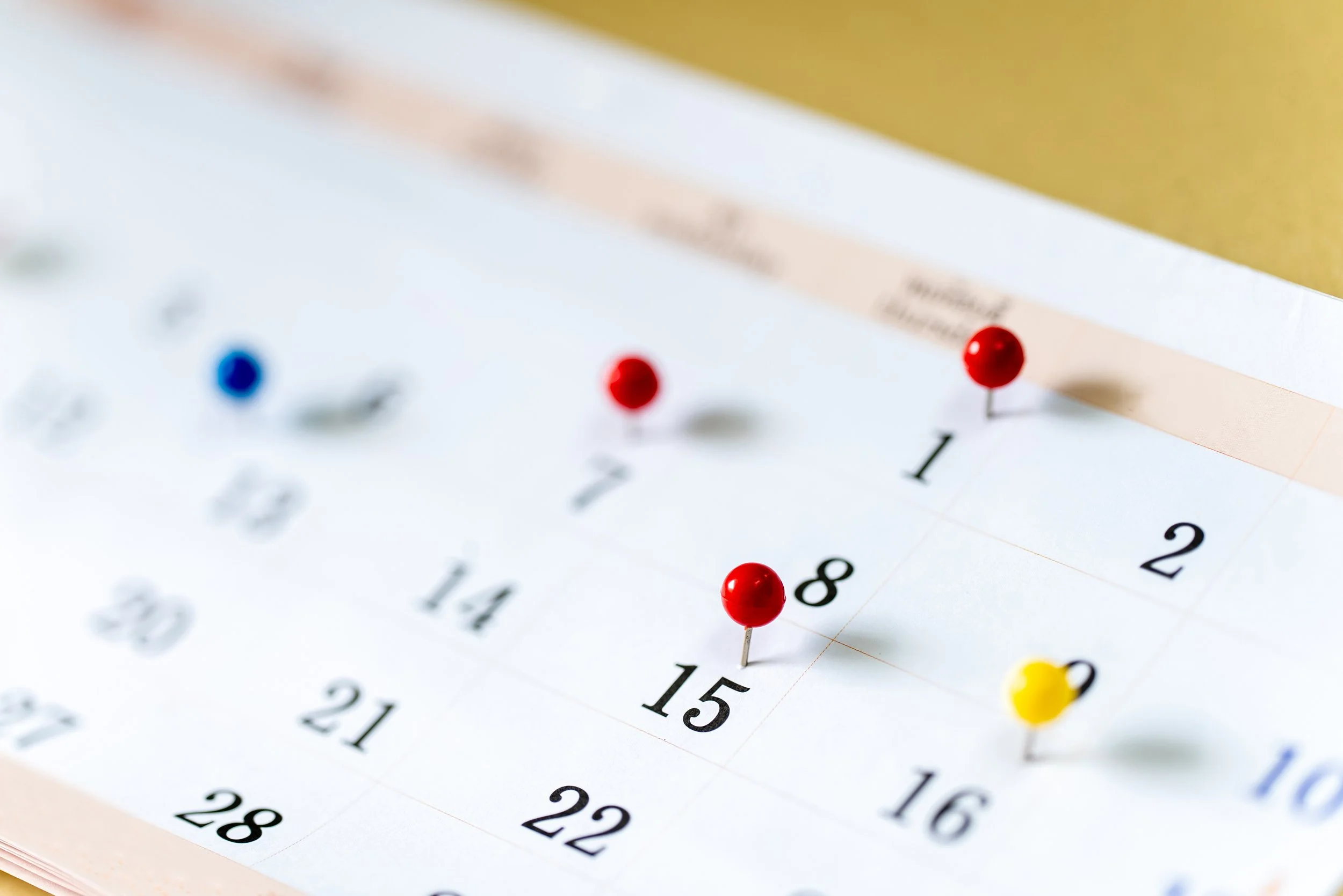 Primer plano de un calendario con chinchetas de colores en determinados días.