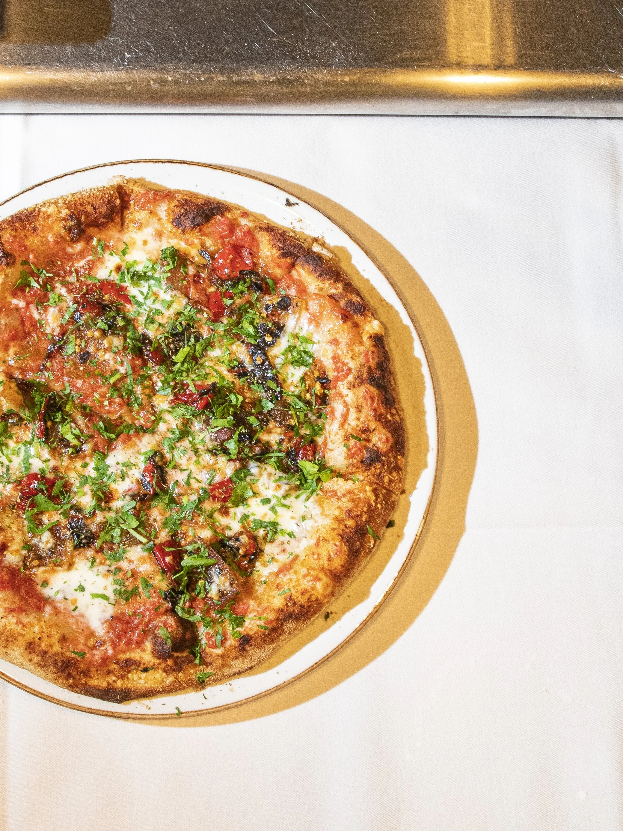 A top-down view of a pizza with cheese, tomato sauce, herbs, and chopped vegetables on a white plate.